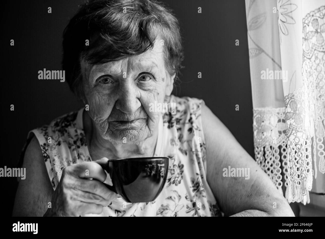 Portrait d'une vieille femme pensionnée assis à une table dans sa maison. Photo en noir et blanc. Banque D'Images
