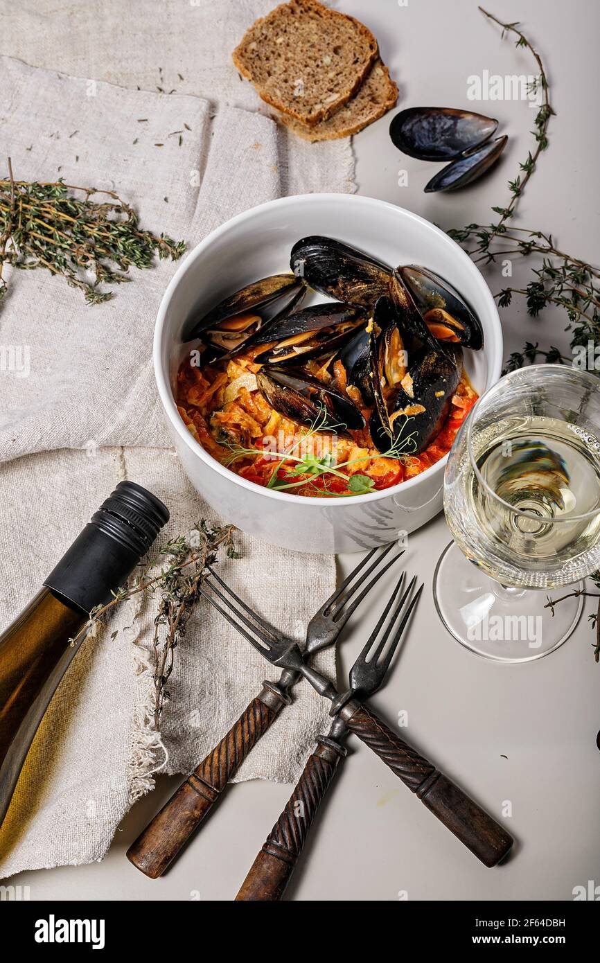 Moules aux légumes, serviette en lin léger, fourchettes millésimes et branches d'origan sur fond clair. Bouteille et verre de vin blanc sec. Délicieux et Banque D'Images