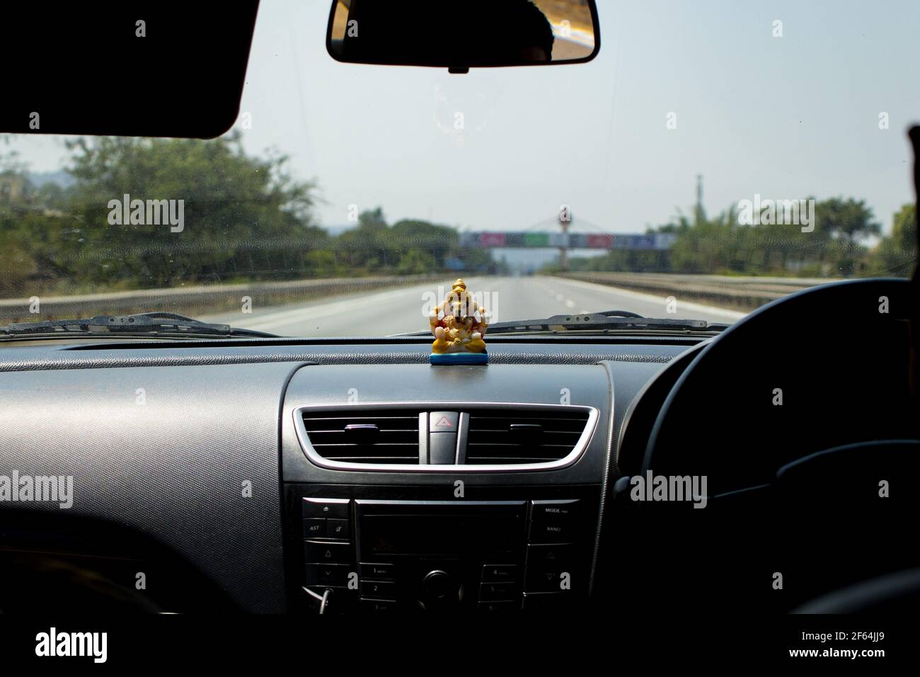 Tableau de bord de voiture avec statue de Ganesha avec voie rapide vide regarder à travers un pare-brise de voiture avec petite statue de dieu sur le tableau de bord le soleil ou le soleil Banque D'Images