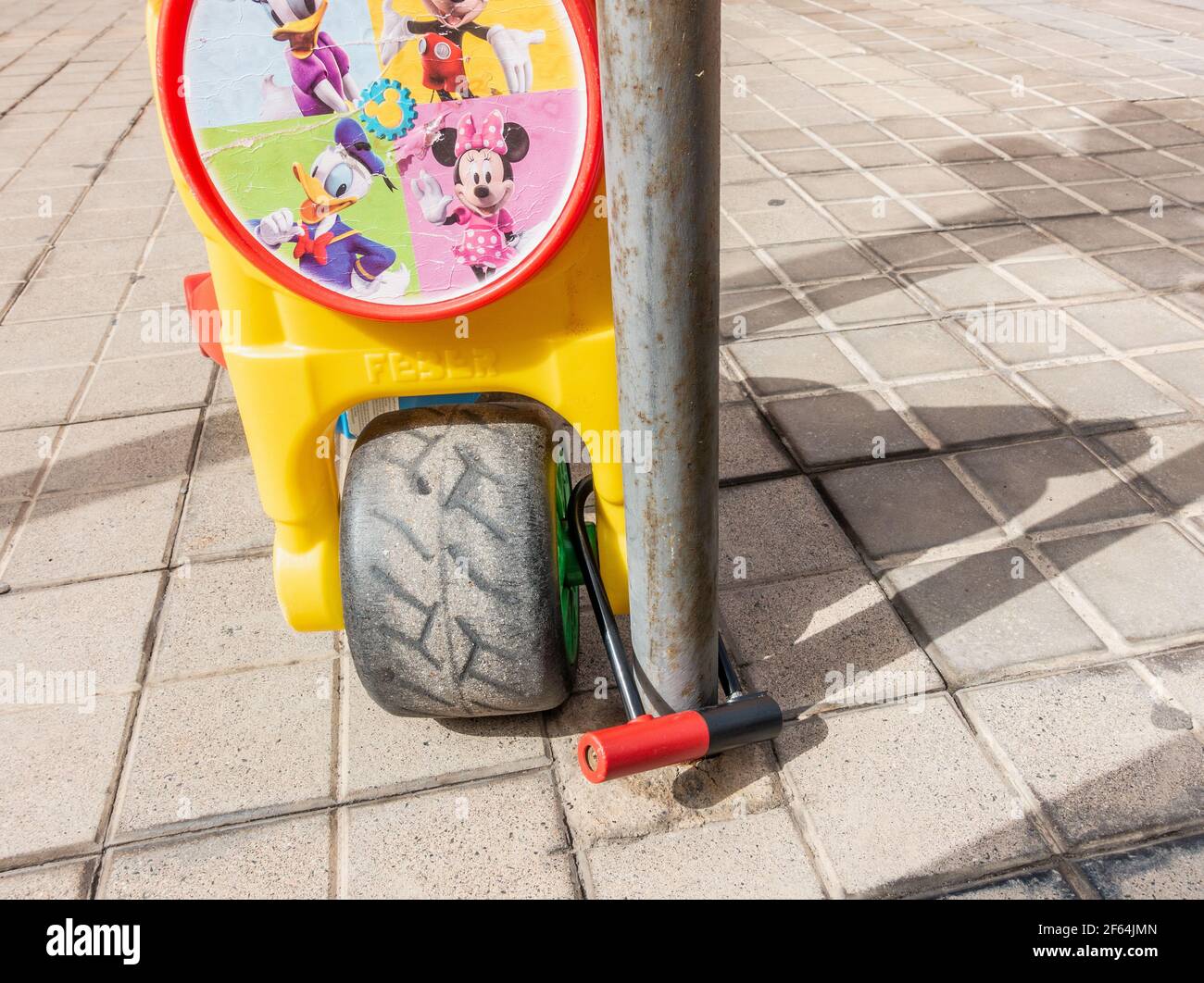 Vélo en plastique pour enfants verrouillé avec un cadenas en U pour service intensif poteau de parc à vélo à l'extérieur de l'école junior Banque D'Images