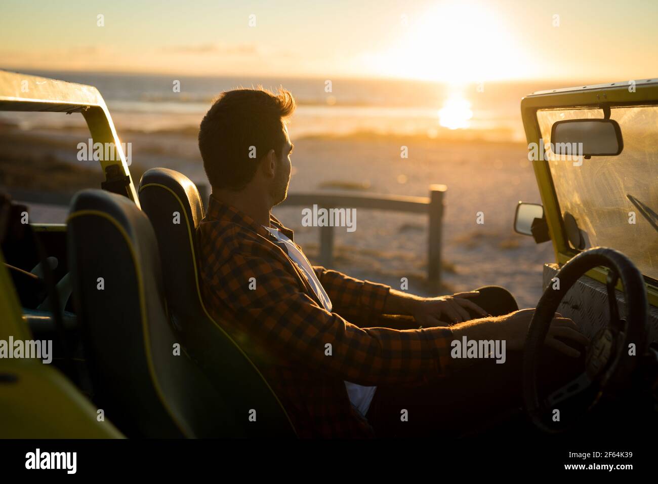 Homme caucasien assis à bord de la plage buggy au bord de la mer pendant coucher de soleil Banque D'Images