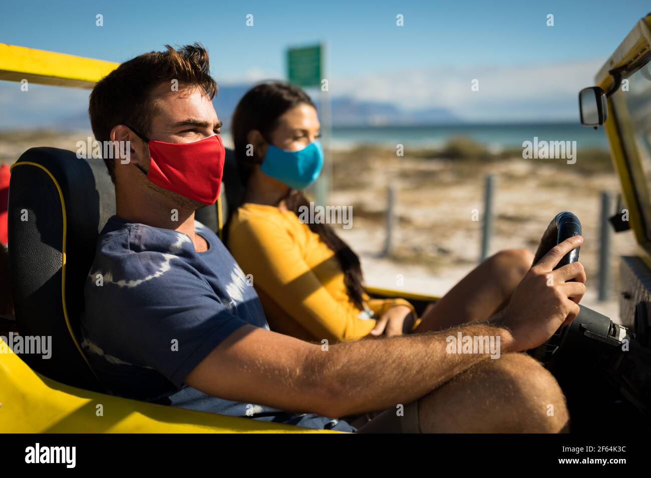 Heureux couple caucasien portant des masques de visage assis dans la buggy de plage Banque D'Images
