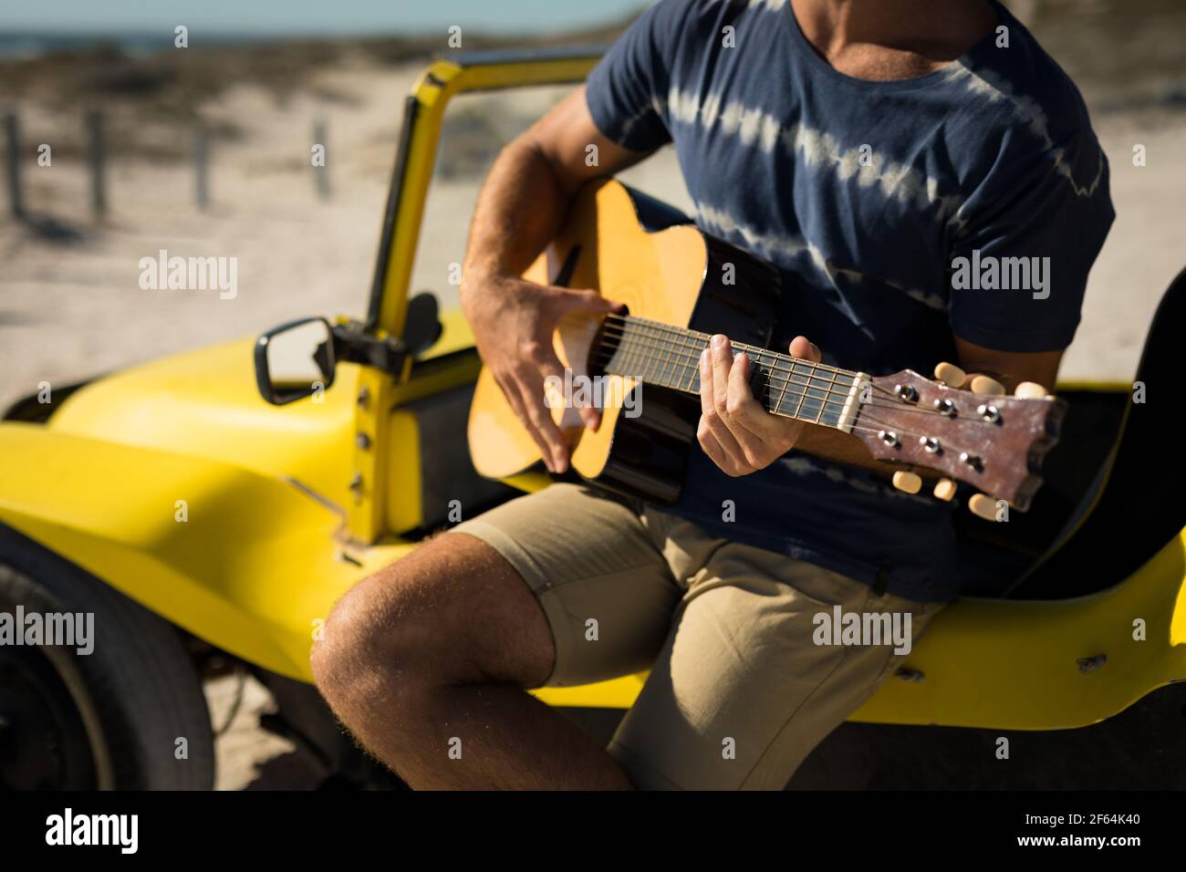 Mi-section de l'homme caucasien assis sur la plage buggy jouant de la guitare Banque D'Images