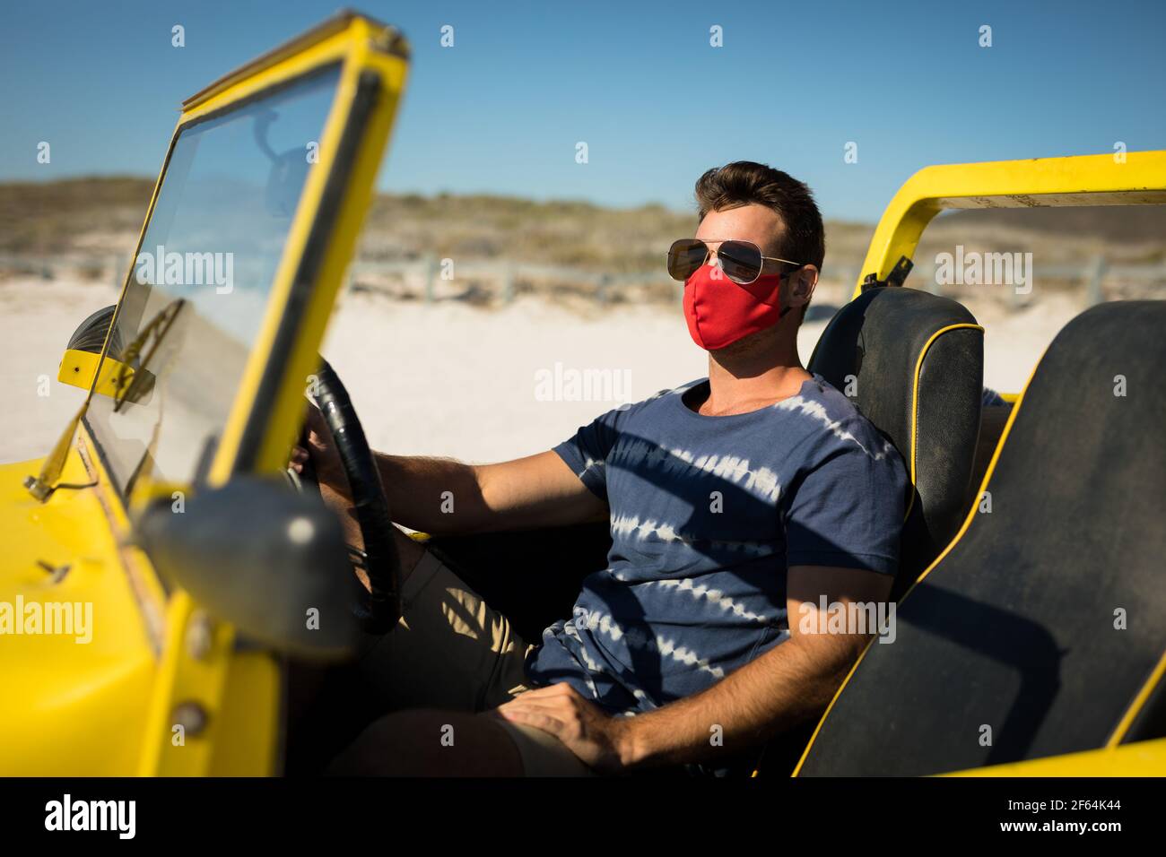 Homme caucasien portant un masque facial et des lunettes de soleil assis à la plage buggy Banque D'Images