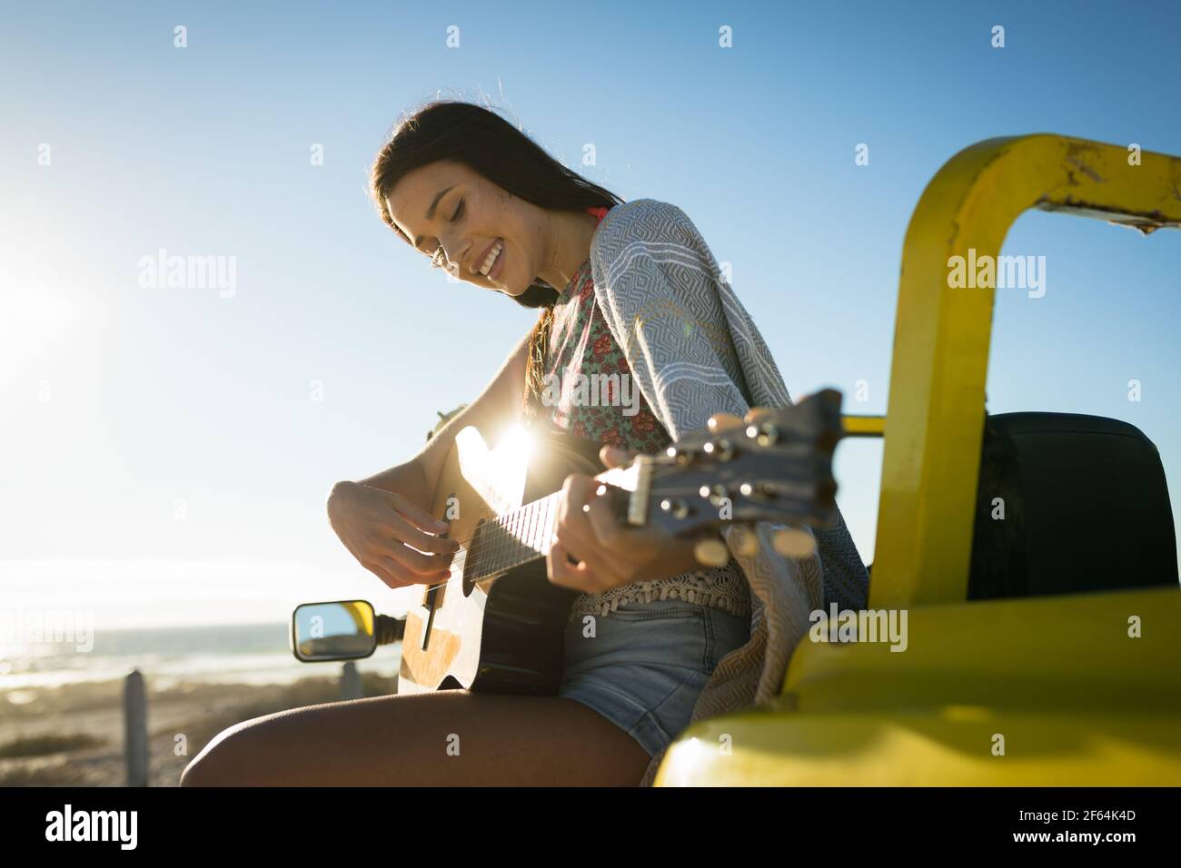 Bonne femme caucasienne assise sur une promenade de plage au bord de la mer jouer de la guitare Banque D'Images