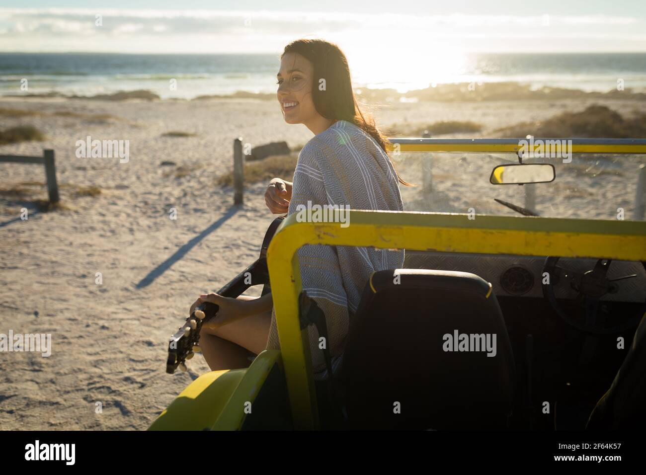 Bonne femme caucasienne assise sur une promenade de plage au bord de la mer jouer de la guitare Banque D'Images