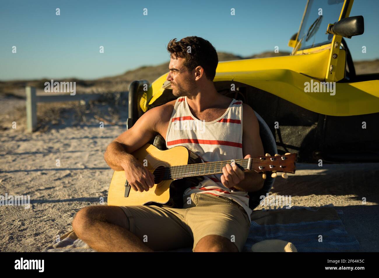 Un homme caucasien heureux s'est penché contre la promenade de la plage au bord de la mer jouer de la guitare Banque D'Images