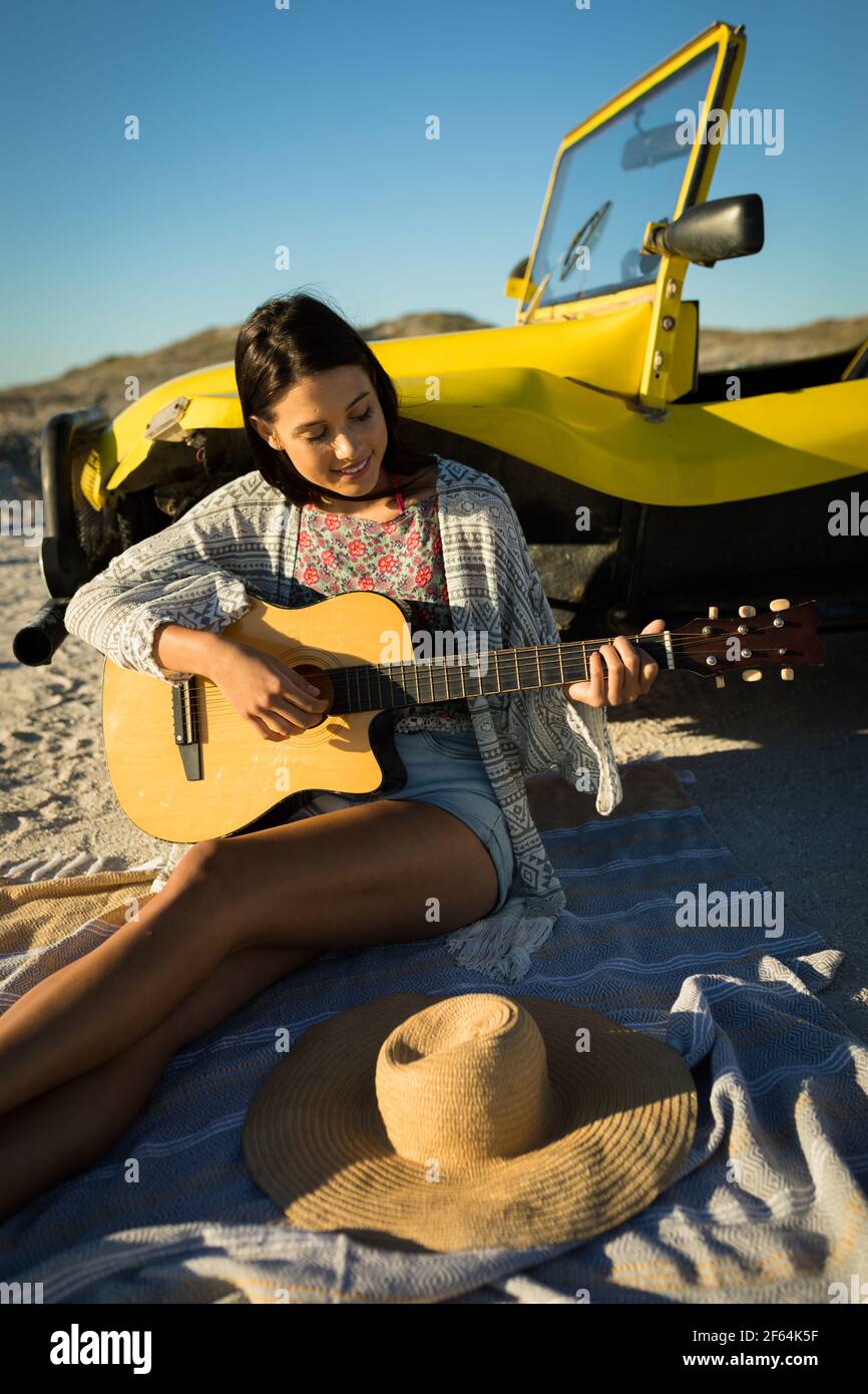 Bonne femme caucasienne s'est penchée contre le buggy de plage au bord de la mer jouer de la guitare Banque D'Images
