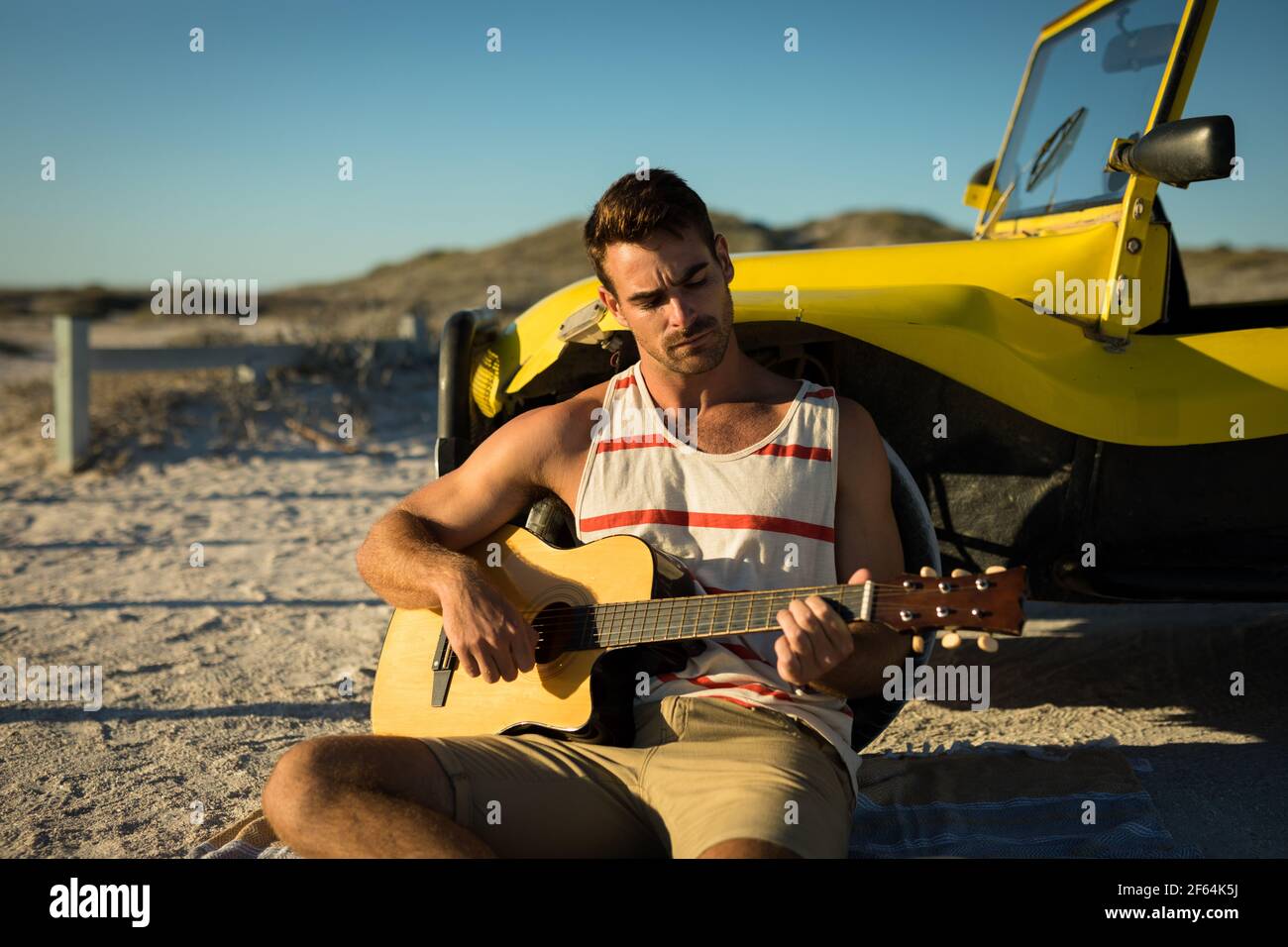 Un homme caucasien heureux s'est penché contre la promenade de la plage au bord de la mer jouer de la guitare Banque D'Images