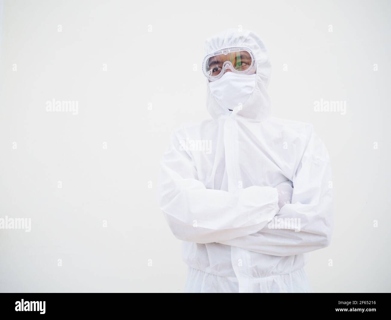 Portrait d'un homme asiatique confiant médecin ou scientifique dans l'uniforme de la suite PPE tout en repliant ses mains dans le fond blanc. Coronavirus ou COVID-19 con Banque D'Images