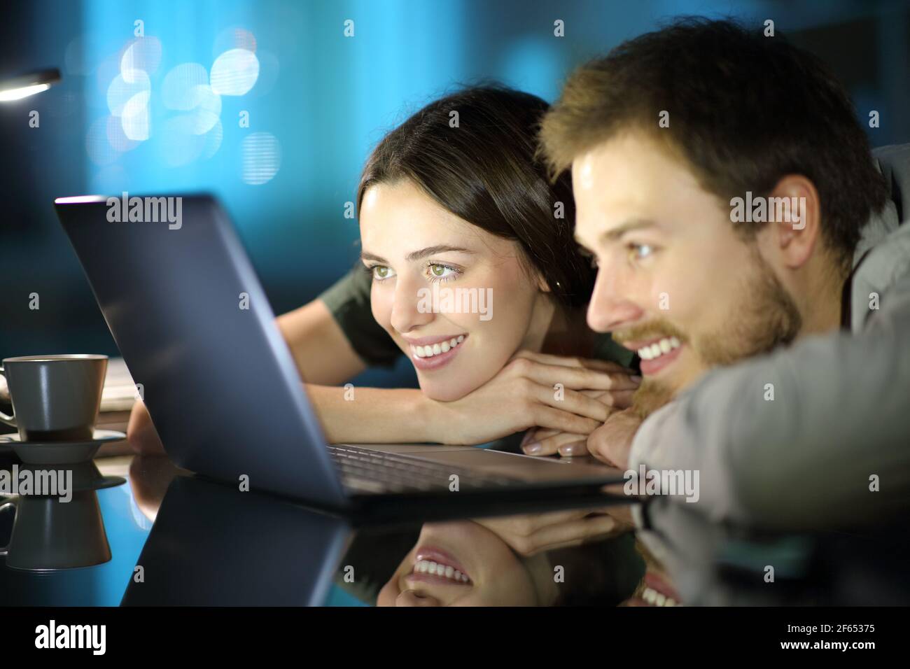 Couple heureux de regarder du contenu multimédia sur un ordinateur portable dans la nuit à la maison Banque D'Images