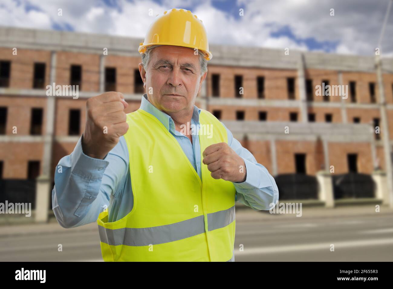 Un vieil homme en colère dans une tenue de travail portant un gilet  fluorescent et un casque de sécurité jaune montrant les poings comme une  boxe agressive création de gestes b Photo