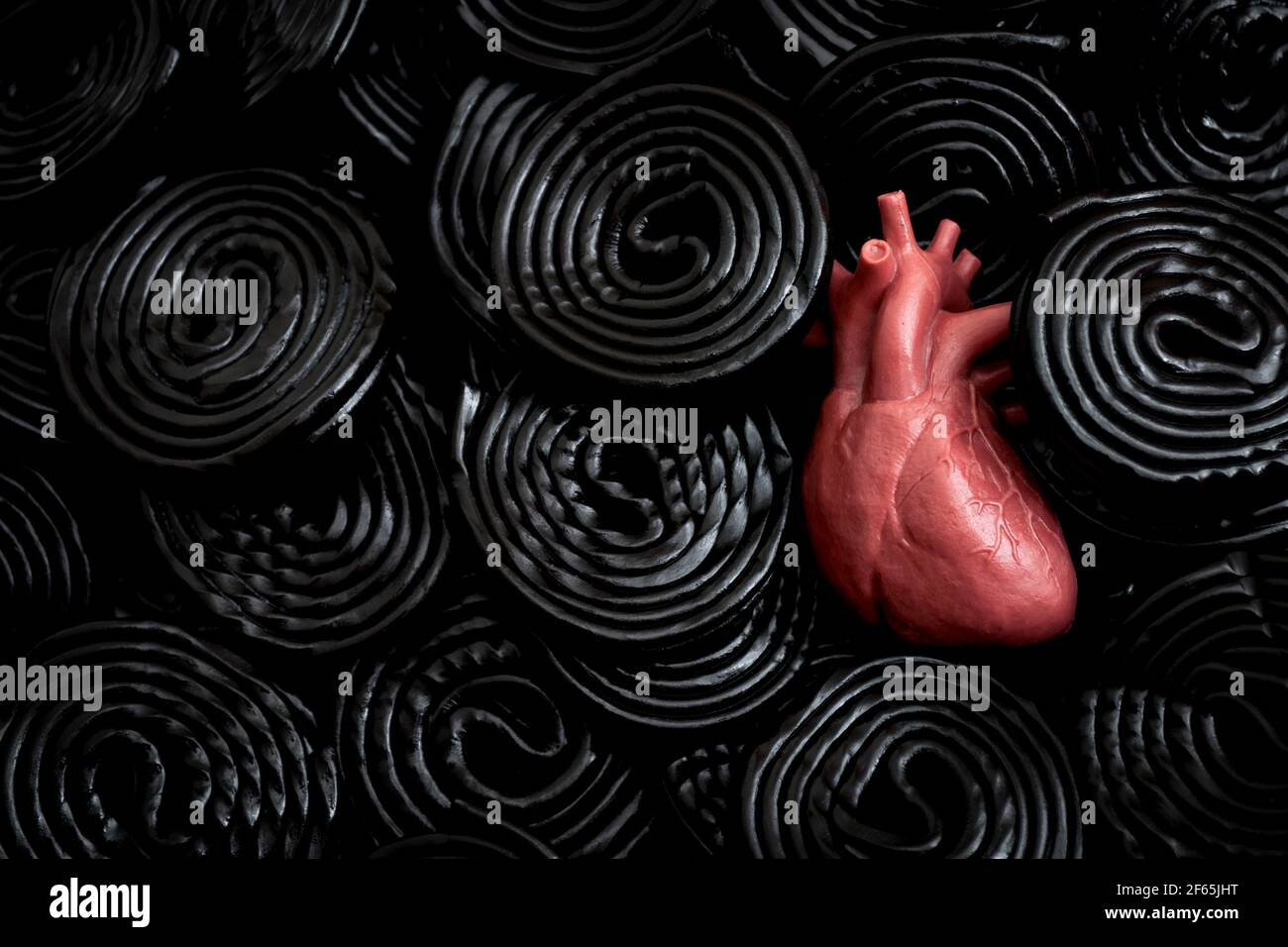La réglisse noire est mauvaise pour votre concept de santé avec un coeur enfoui dans les roues de réglisse qui contiennent le composé édulcorant glycyrrhizine, qui peut déc Banque D'Images