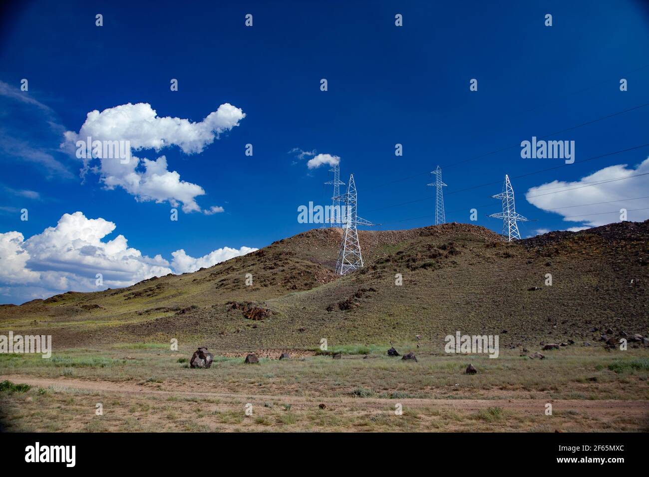Mâts de ligne de transmission de puissance argent (pylônes électriques) et fils sur les collines et ciel bleu profond avec fond de nuages. Banque D'Images