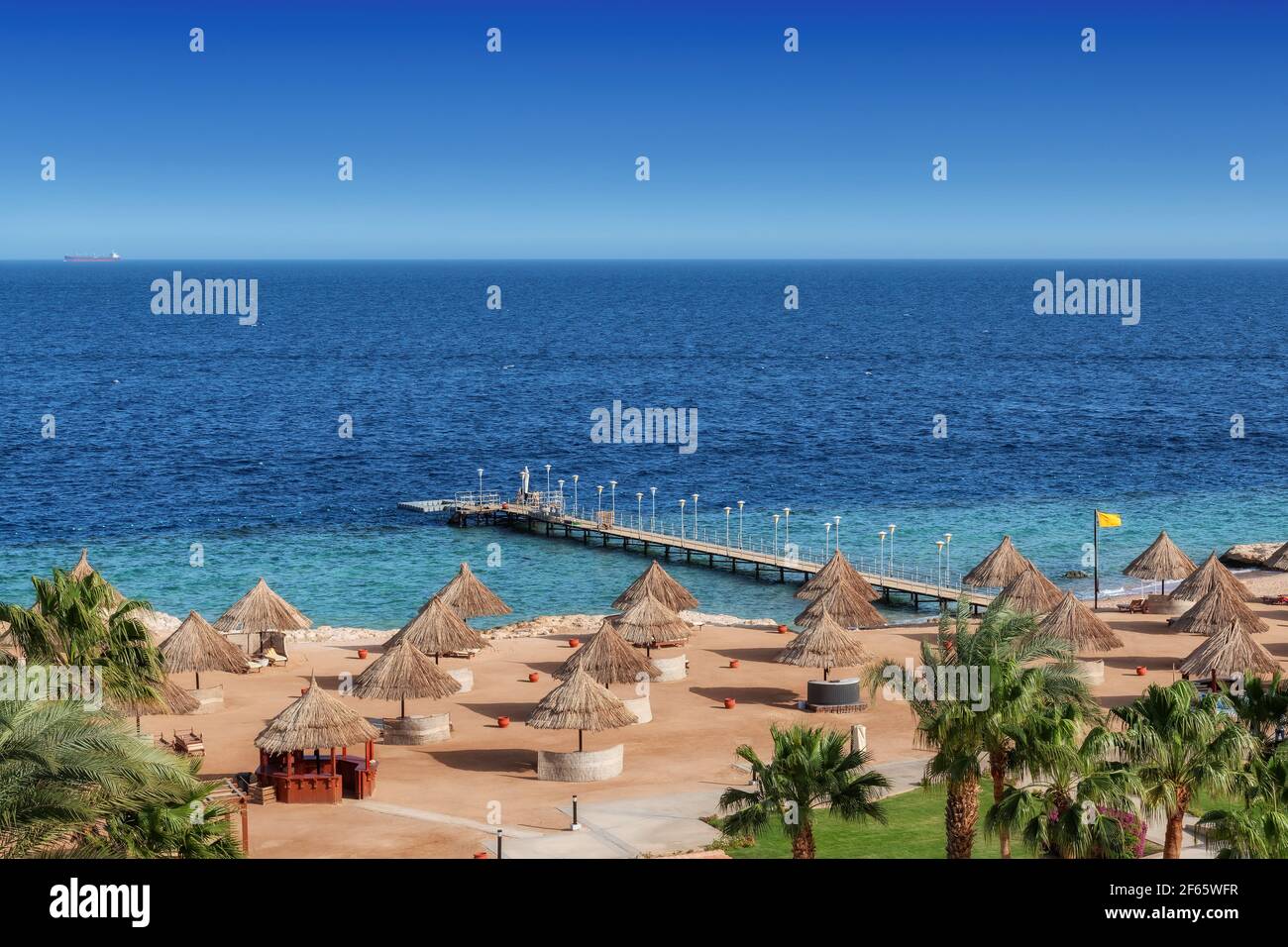 Plage ensoleillée dans un complexe tropical avec palmiers et parasols En Mer Rouge Banque D'Images