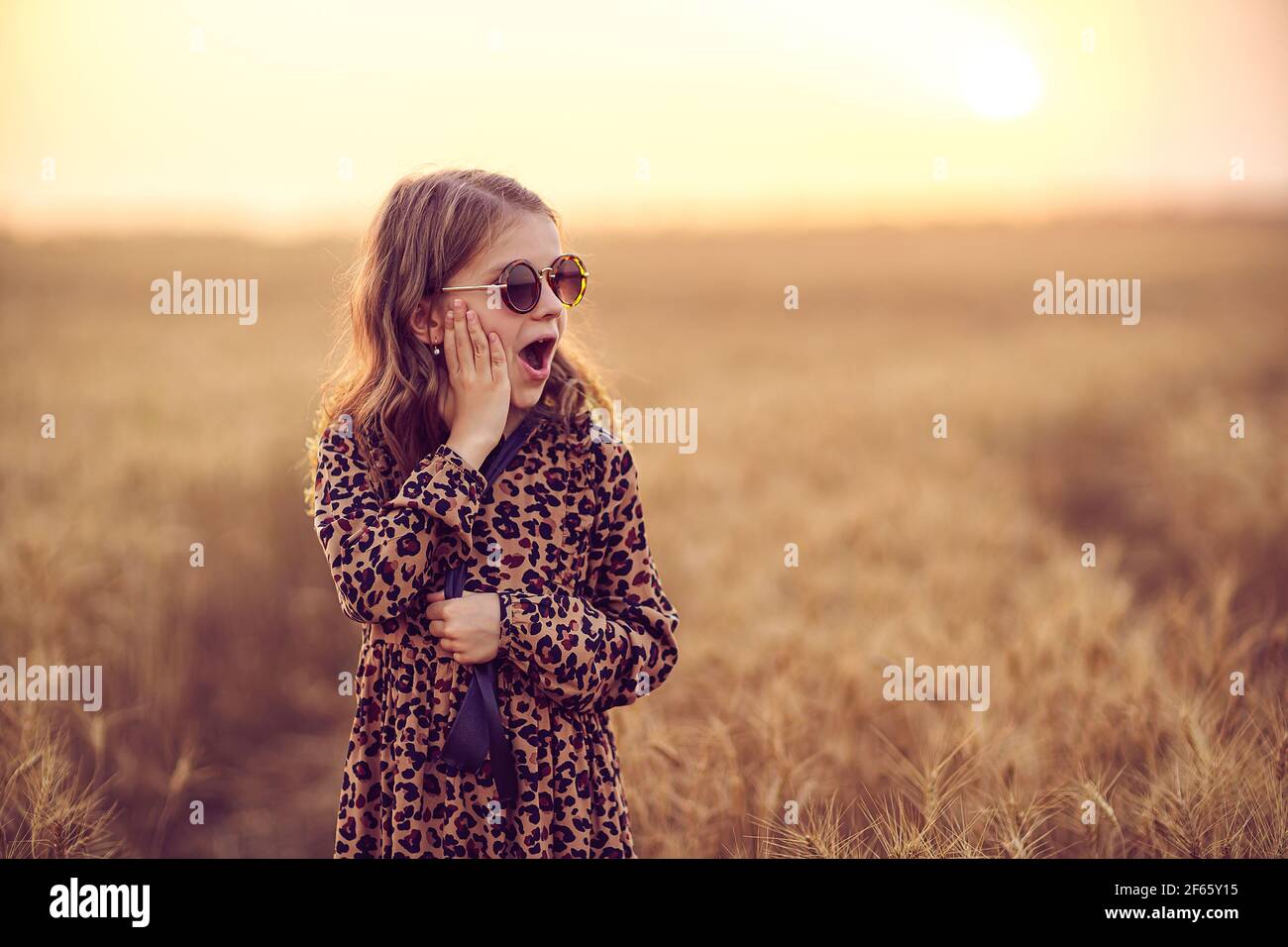 Belle petite fille portant une robe léopard et des lunettes de soleil  arrondies debout dans le champ de blé Photo Stock - Alamy