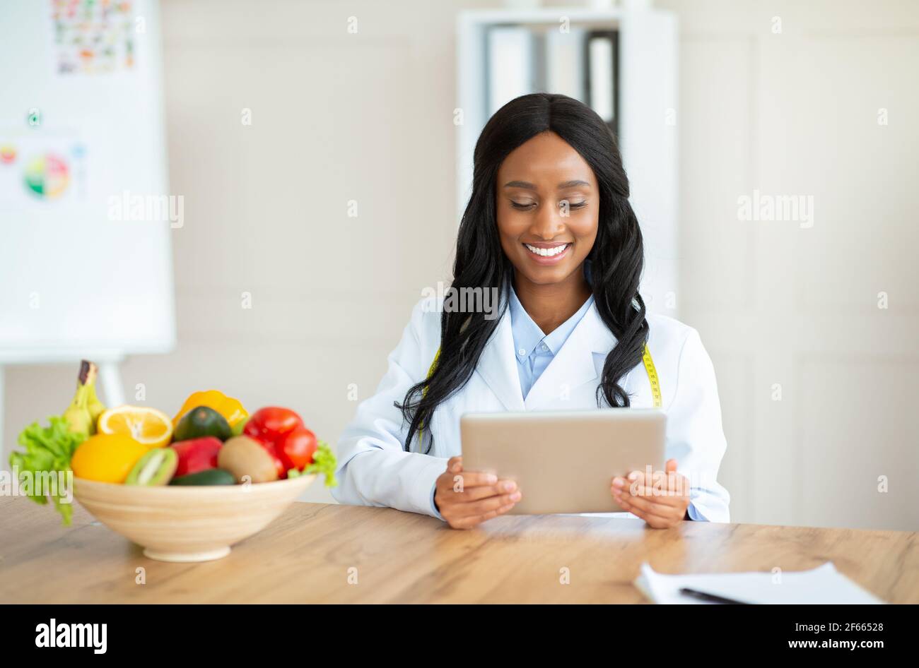 Nutritionniste afro-américain travaillant avec un ordinateur de tablette, donnant consultation en ligne au bureau médical, l'espace de copie Banque D'Images