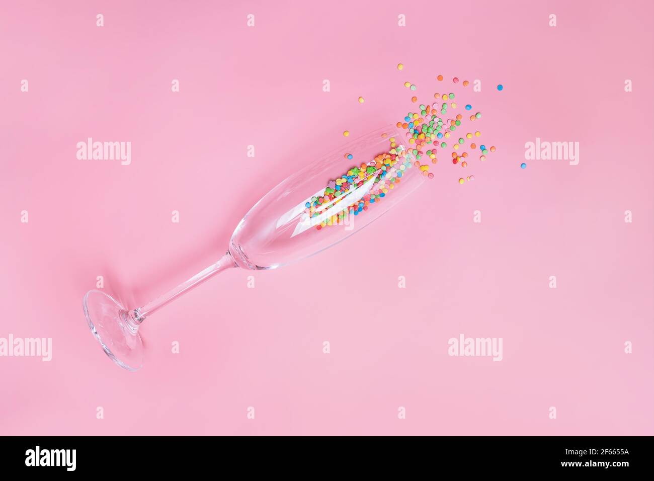 Des bonbons colorés saupoudrent dans un verre de champagne sur fond rose pastel. Banque D'Images