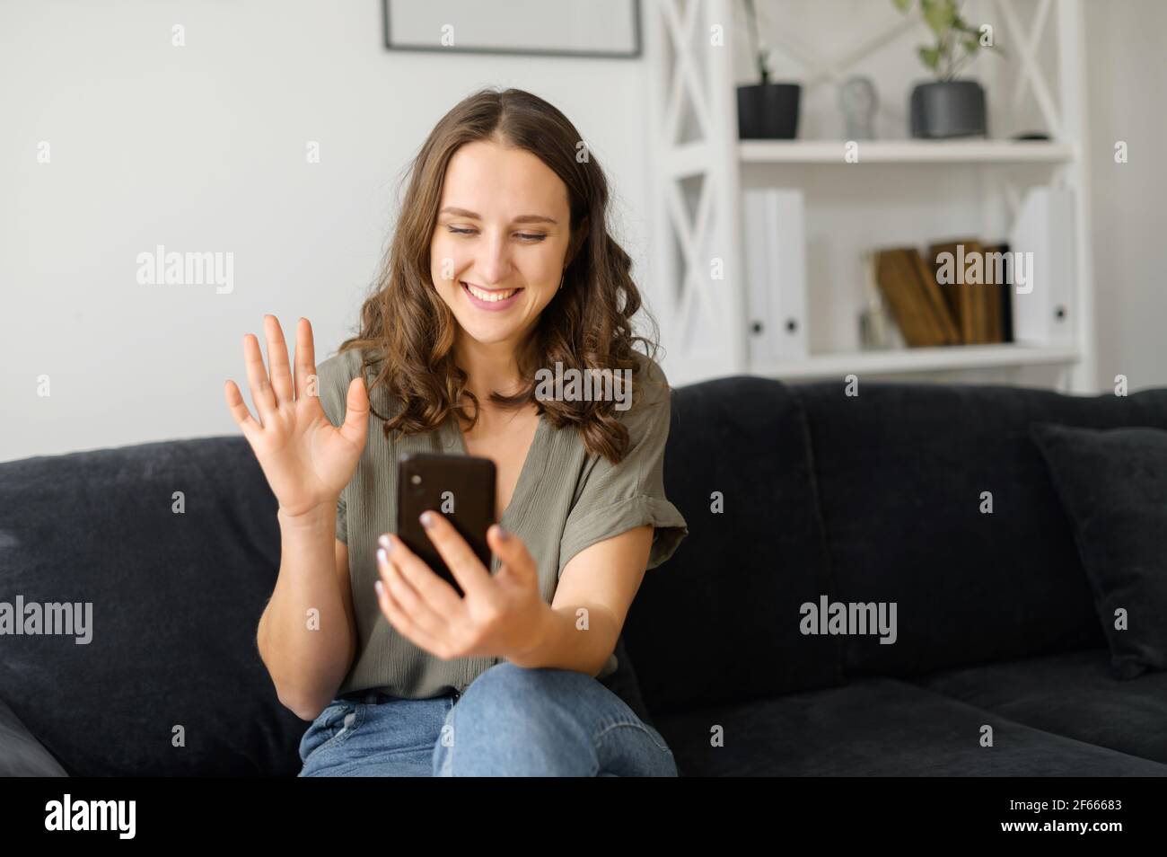 Jeune femme gaie utilisant un téléphone portable pour les appels vidéo,  allongé sur le canapé confortable de la maison, étudiante souriante  discutant en ligne avec des camarades de classe, en faisant passer