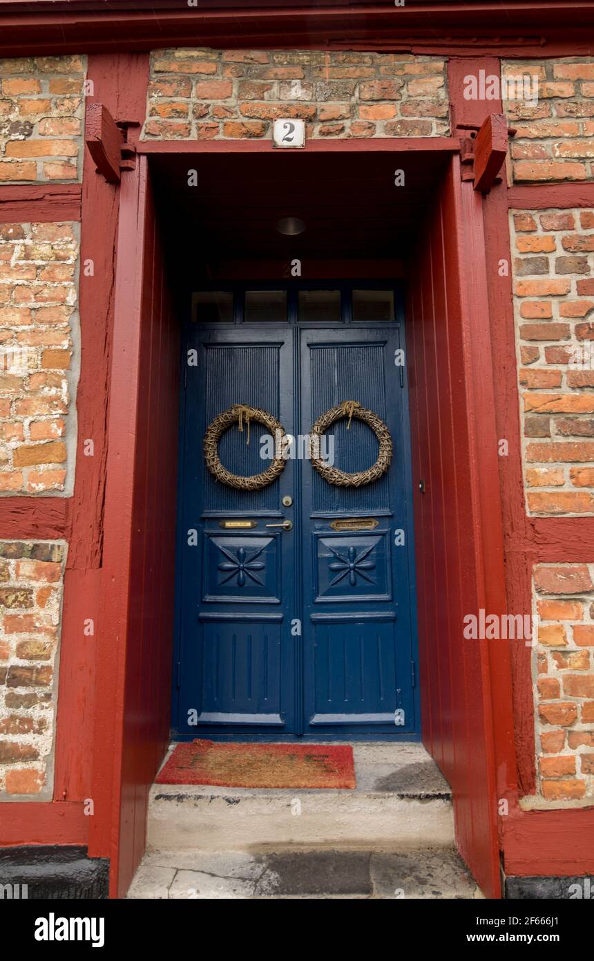 Une vieille maison avec une porte en bois bleu sur laquelle pendent deux couronnes, située dans un cadre en bois peint en rouge près de Stortoget à Ystad, en Suède. Banque D'Images