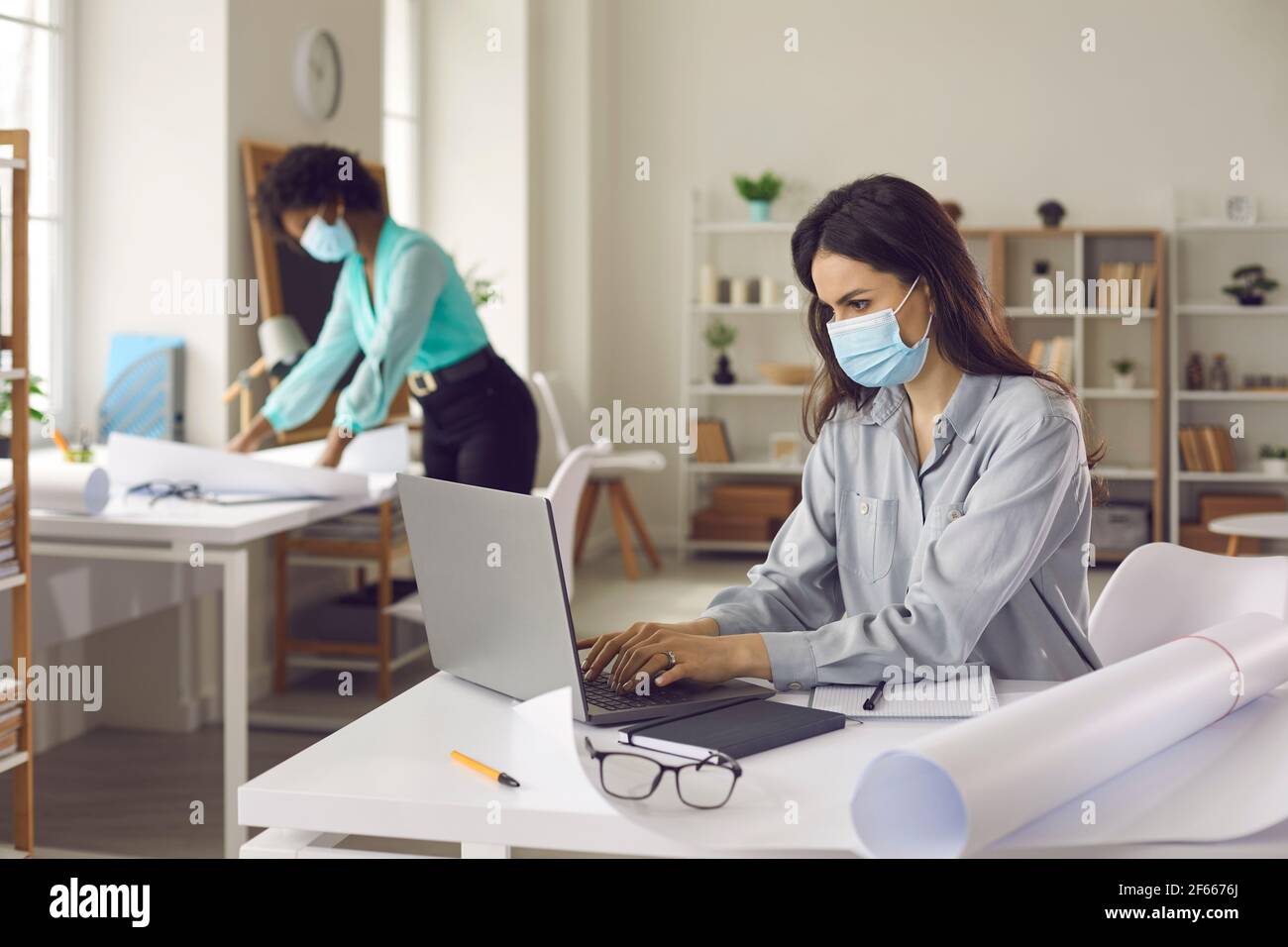 Femme multiethnique collègue dans le masque de visage travaillant dans le bureau garder distance Banque D'Images