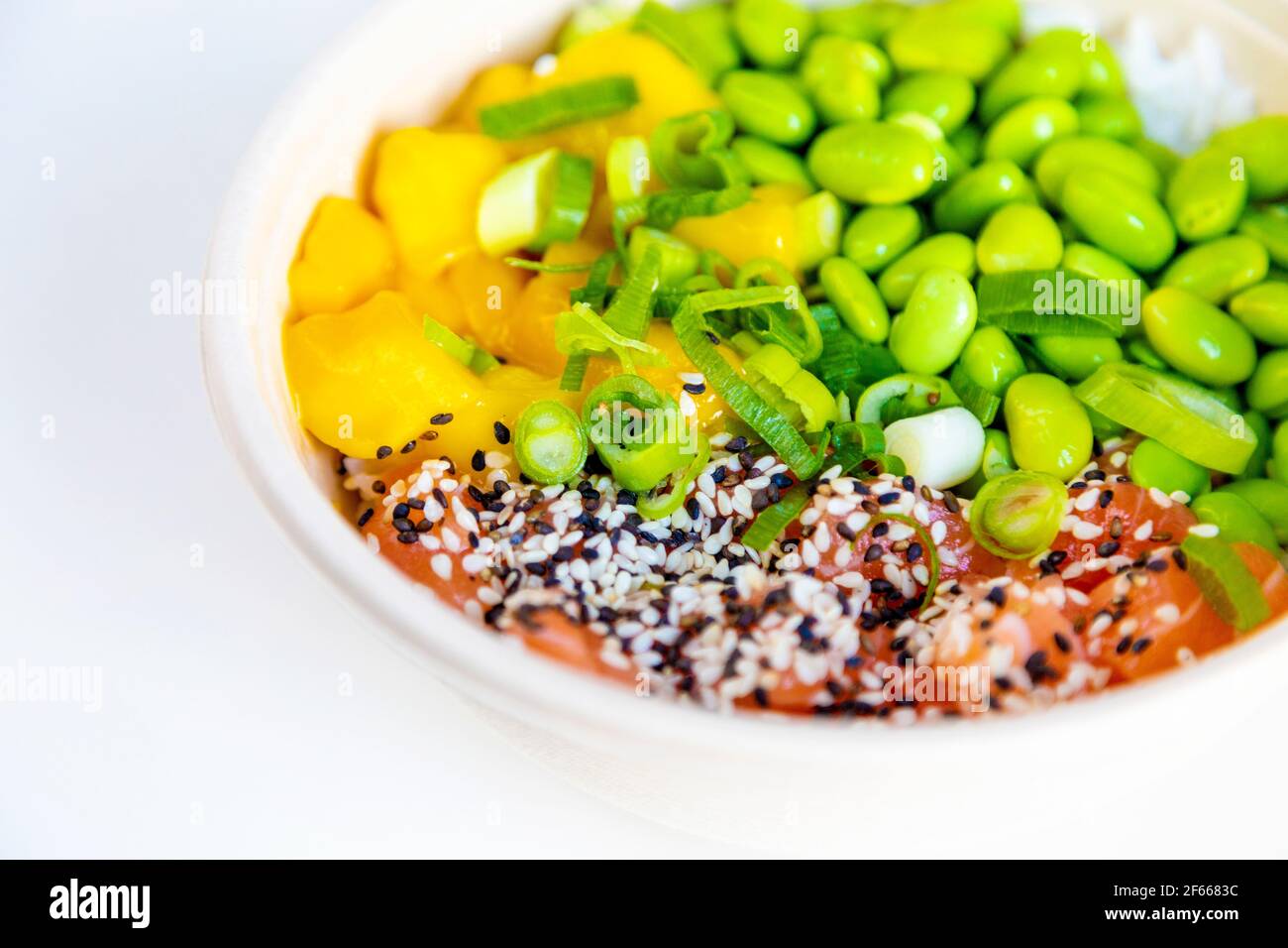 Un bol à poke avec de l'edamame, du saumon, de la mangue, recouvert d'oignons de printemps et de sésame sur un lit de riz Banque D'Images