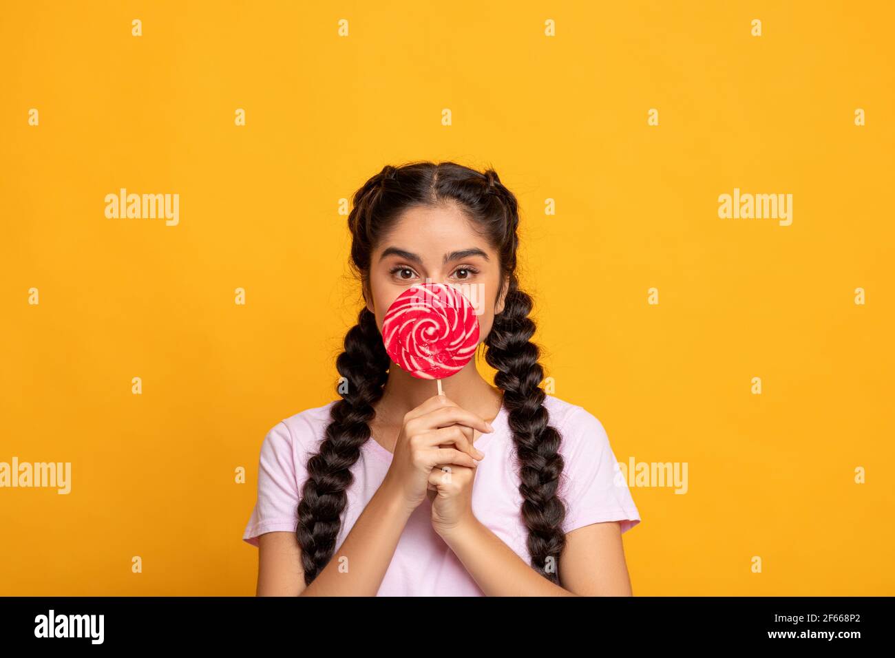 Femme indienne tenant une lollipop, couvrant la bouche avec des bonbons Banque D'Images