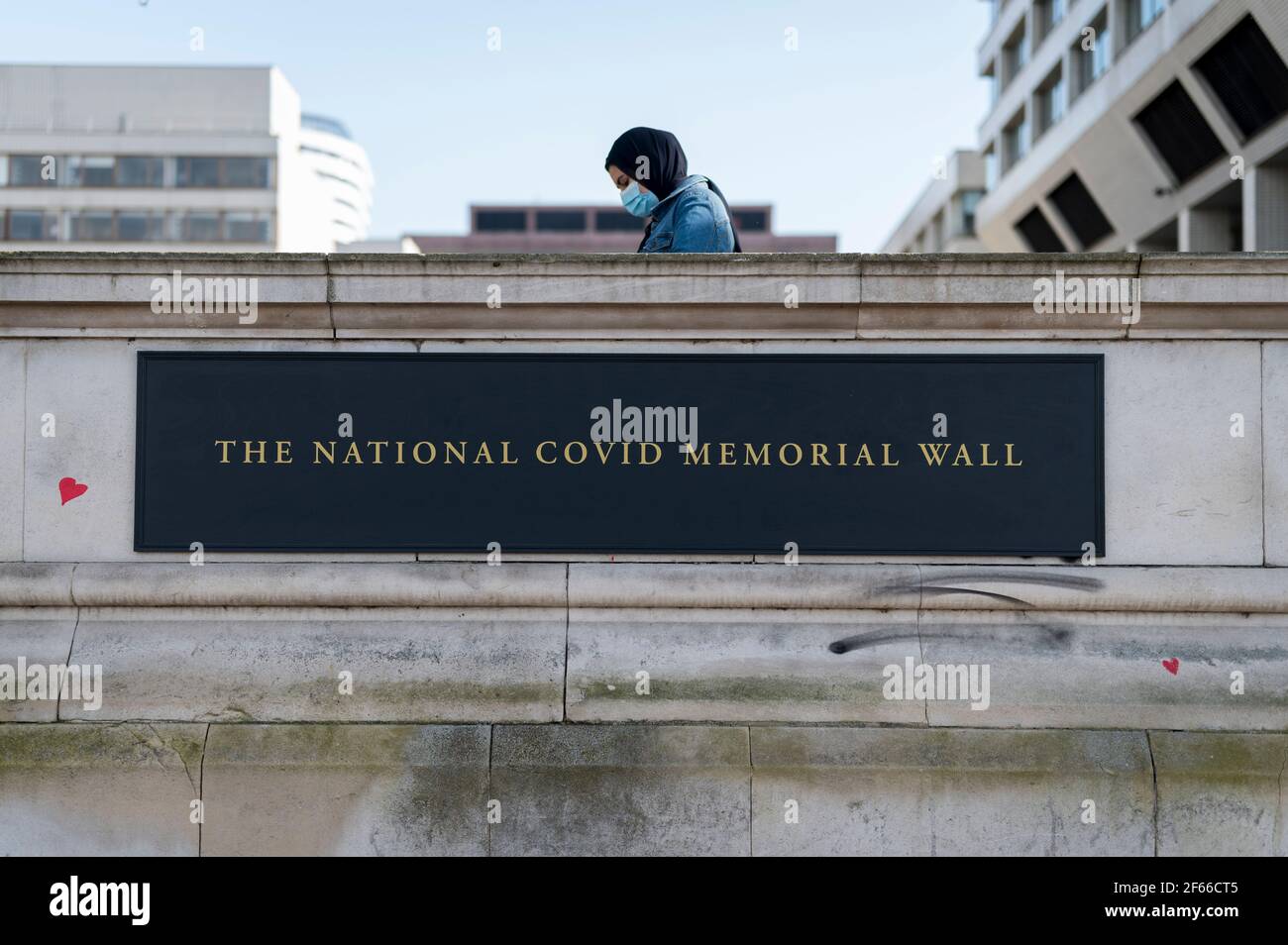 Londres, Royaume-Uni. 30 mars 2021. Une femme dans un masque facial au-dessus d'un panneau pour un mur de cœur au mur commémoratif national Covid de Lambeth, près de la Tamise, chaque cœur représentant quelqu'un qui est décédé pendant la pandémie de coronavirus au Royaume-Uni. Appelé le mur commémoratif national Covid, il a été créé par les familles bereaved Covid-19 pour la justice et s'étendra sur un demi-mile au moment où il sera terminé. Crédit : Stephen Chung/Alay Live News Banque D'Images