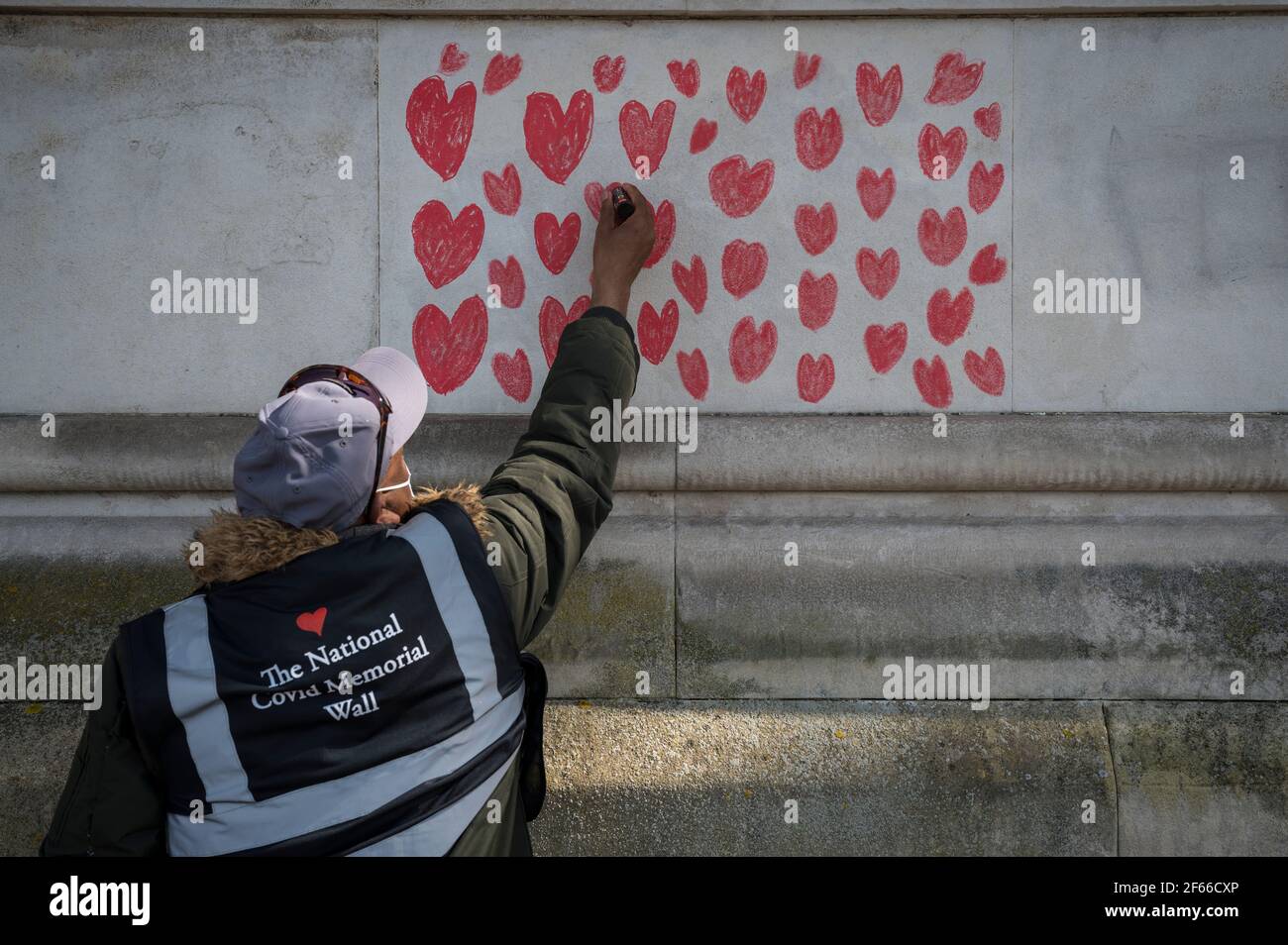 Londres, Royaume-Uni. 30 mars 2021. Un volontaire tire les coeurs sur un mur à Lambeth près de la Tamise, chaque coeur représentant quelqu'un qui est décédé pendant la pandémie de coronavirus au Royaume-Uni. Appelé le mur commémoratif national Covid, il a été créé par les familles bereaved Covid-19 pour la justice et s'étendra sur un demi-mile au moment où il sera terminé. Crédit : Stephen Chung/Alay Live News Banque D'Images