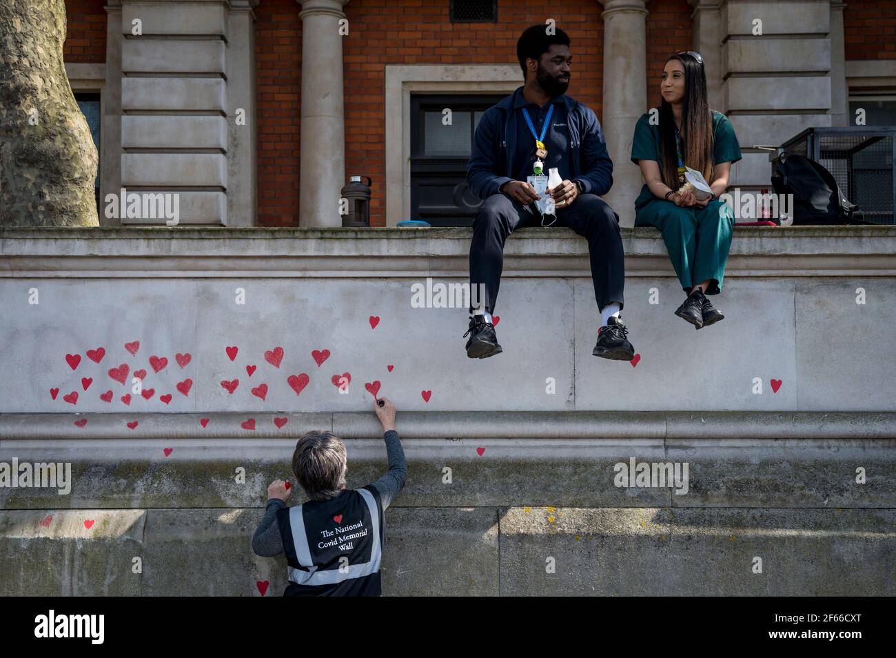 Londres, Royaume-Uni. 30 mars 2021. Les employés du NHS, au-dessus d'un bénévole, attirent les cœurs sur un mur à Lambeth, près de la Tamise, chaque cœur représentant une personne décédée pendant la pandémie de coronavirus au Royaume-Uni. Appelé le mur commémoratif national Covid, il a été créé par les familles bereaved Covid-19 pour la justice et s'étendra sur un demi-mile au moment où il sera terminé. Crédit : Stephen Chung/Alay Live News Banque D'Images