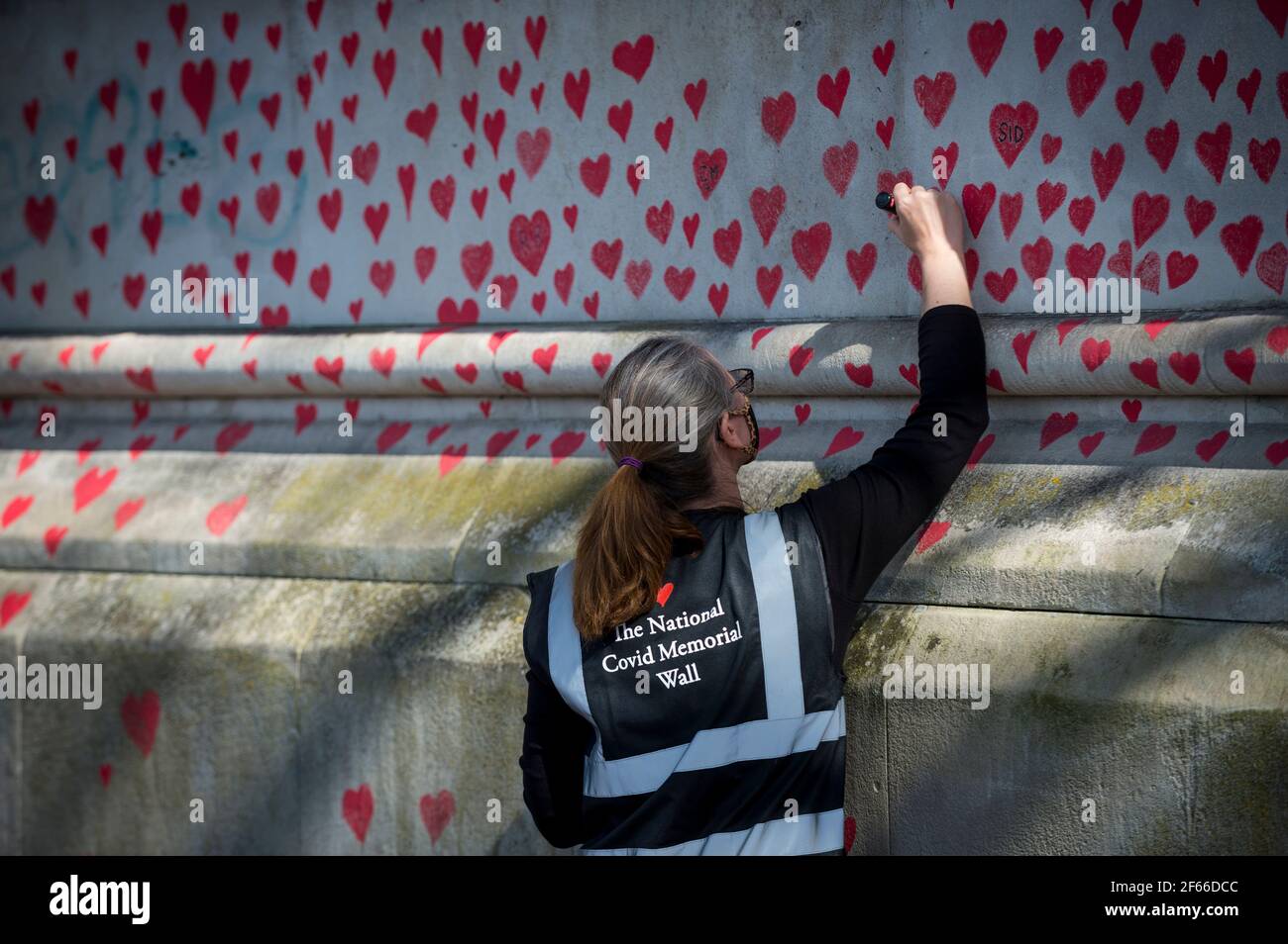 Londres, Royaume-Uni. 30 mars 2021. Un volontaire tire les coeurs sur un mur à Lambeth près de la Tamise, chaque coeur représentant quelqu'un qui est décédé pendant la pandémie de coronavirus au Royaume-Uni. Appelé le mur commémoratif national Covid, il a été créé par les familles bereaved Covid-19 pour la justice et s'étendra sur un demi-mile au moment où il sera terminé. Crédit : Stephen Chung/Alay Live News Banque D'Images