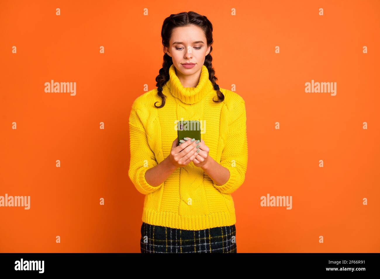 Photo de joli jeune look mains tenir le téléphone port pull knitter isolé sur fond orange Banque D'Images