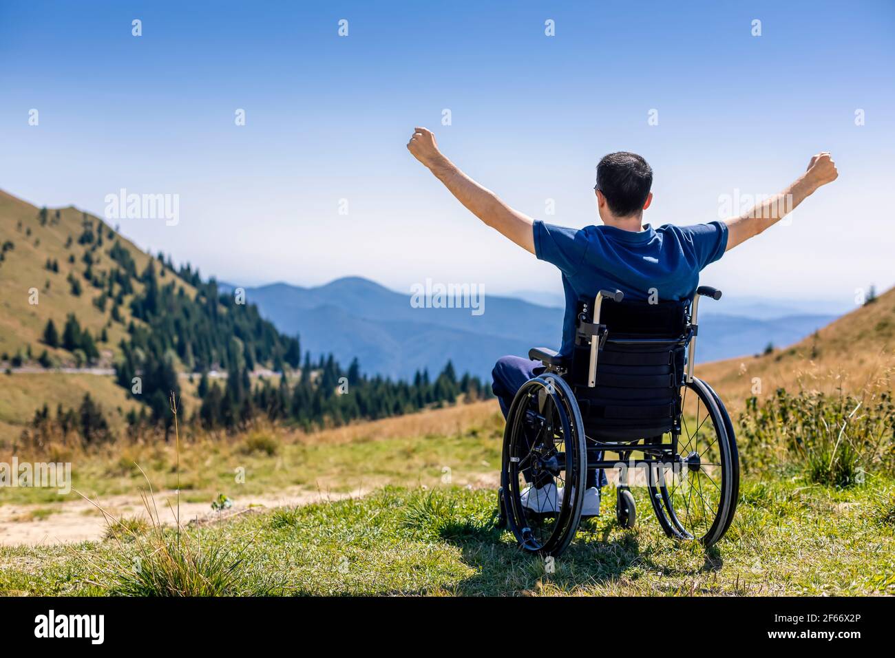 Jeune homme en fauteuil roulant appréciant l'air frais dans une journée ensoleillée sur la montagne Banque D'Images