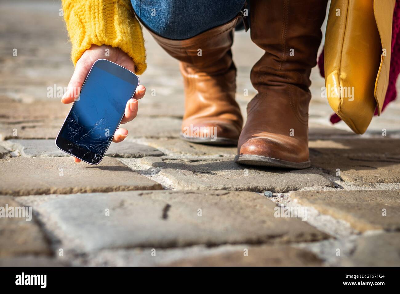 Femme qui prend un smartphone cassé avec un écran tactile fissuré dans la rue. Écran fragile endommagé sur le téléphone portable. Banque D'Images