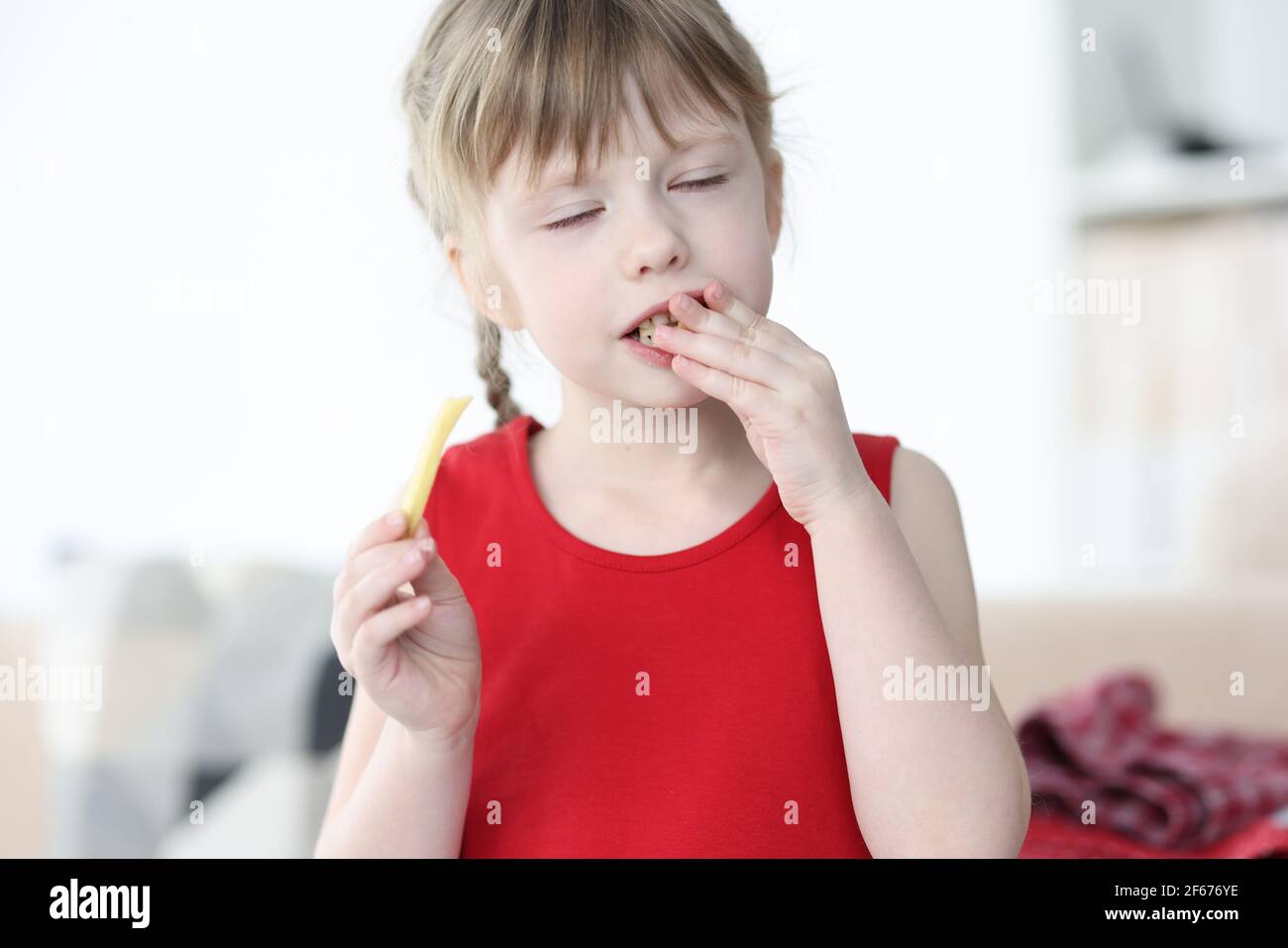 Petite fille aux yeux fermés mangeant de délicieuses frites Banque D'Images