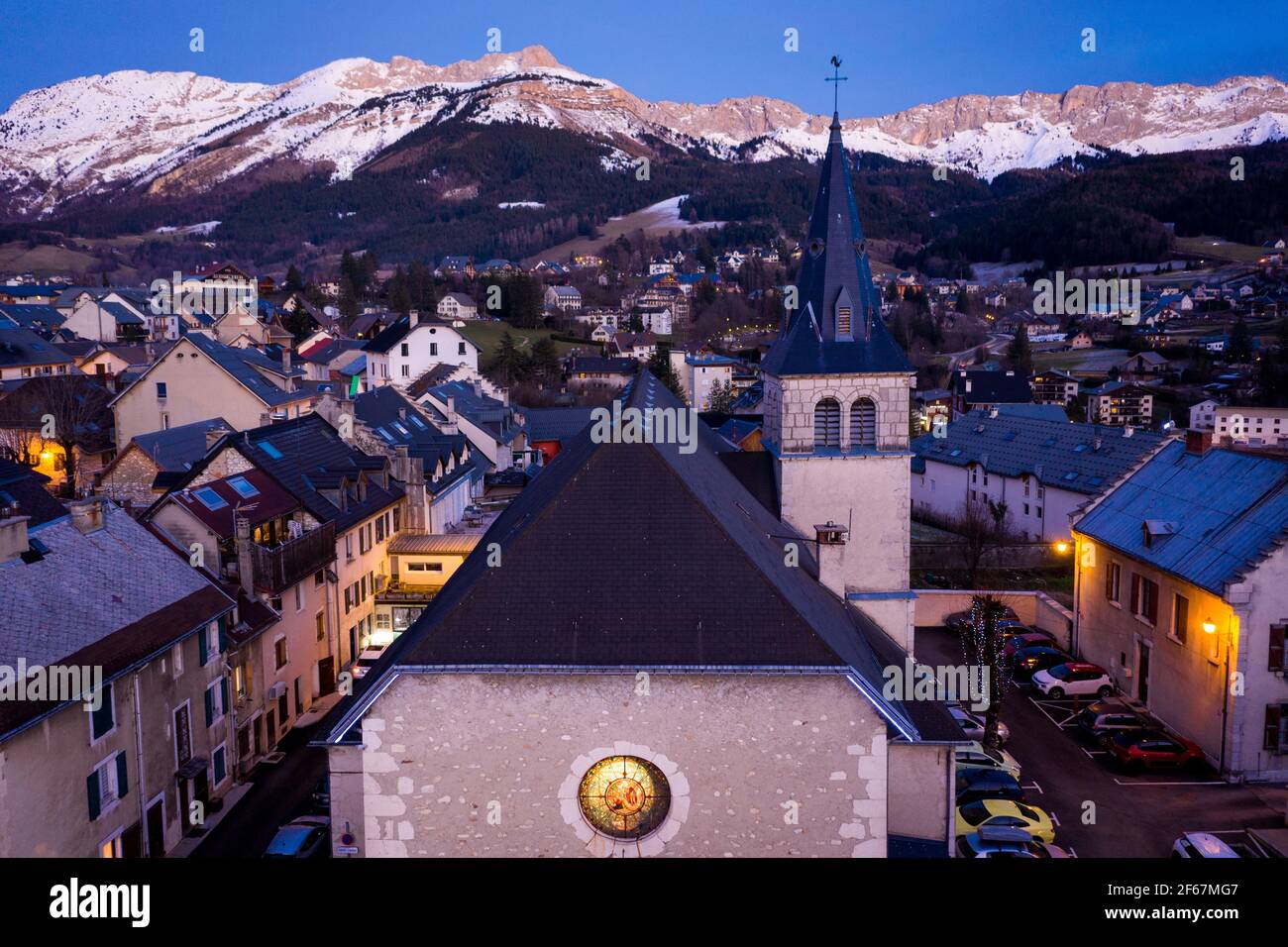 Vue aérienne de l'église avec tour dans le petit village en soirée. Montagnes enneigées à l'horizon, Vercors, France. Banque D'Images