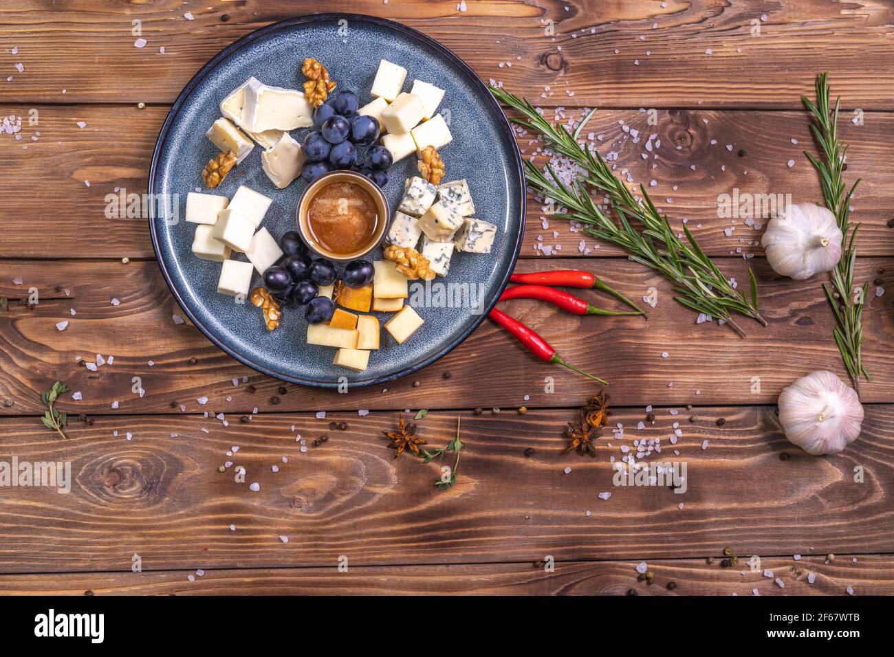 Une assiette de fromage en tranches, miel, raisins sur fond de bois, décorée d'épices, romarin, ail. Service de restaurant. Banque D'Images