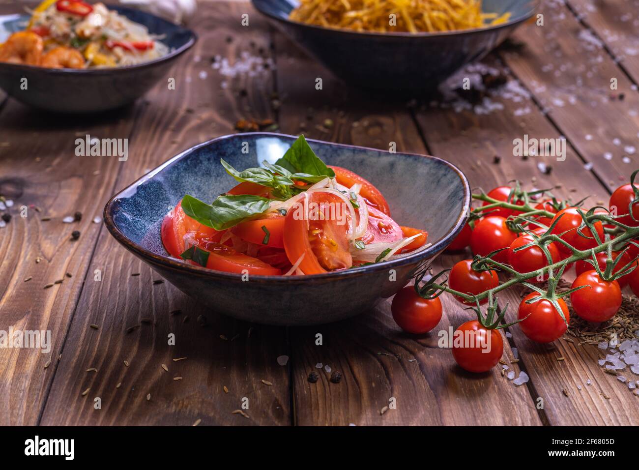 Émincez les tomates avec les oignons dans une assiette sur fond de bois brun, décorée de tomates cerises, de gros sel et de petits pois au poivre. Le concept de la santé Banque D'Images
