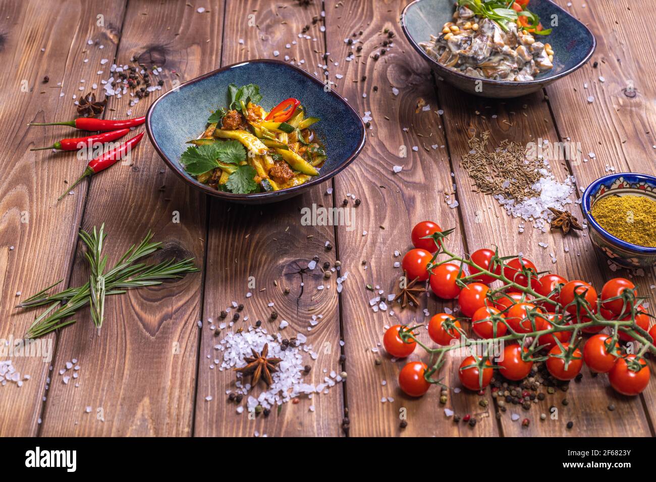 Salades de légumes dans des assiettes, tomates cerises, cannelle, romarin sur fond de bois brun. Le concept de service de restaurant. Banque D'Images