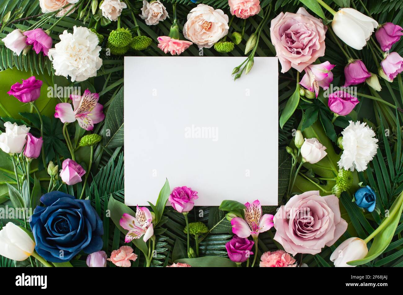 Mise en page créative composée de fleurs d'été colorées et de feuilles vertes avec une note en papier. Fond créatif d'invitation de fleur de printemps. Banque D'Images