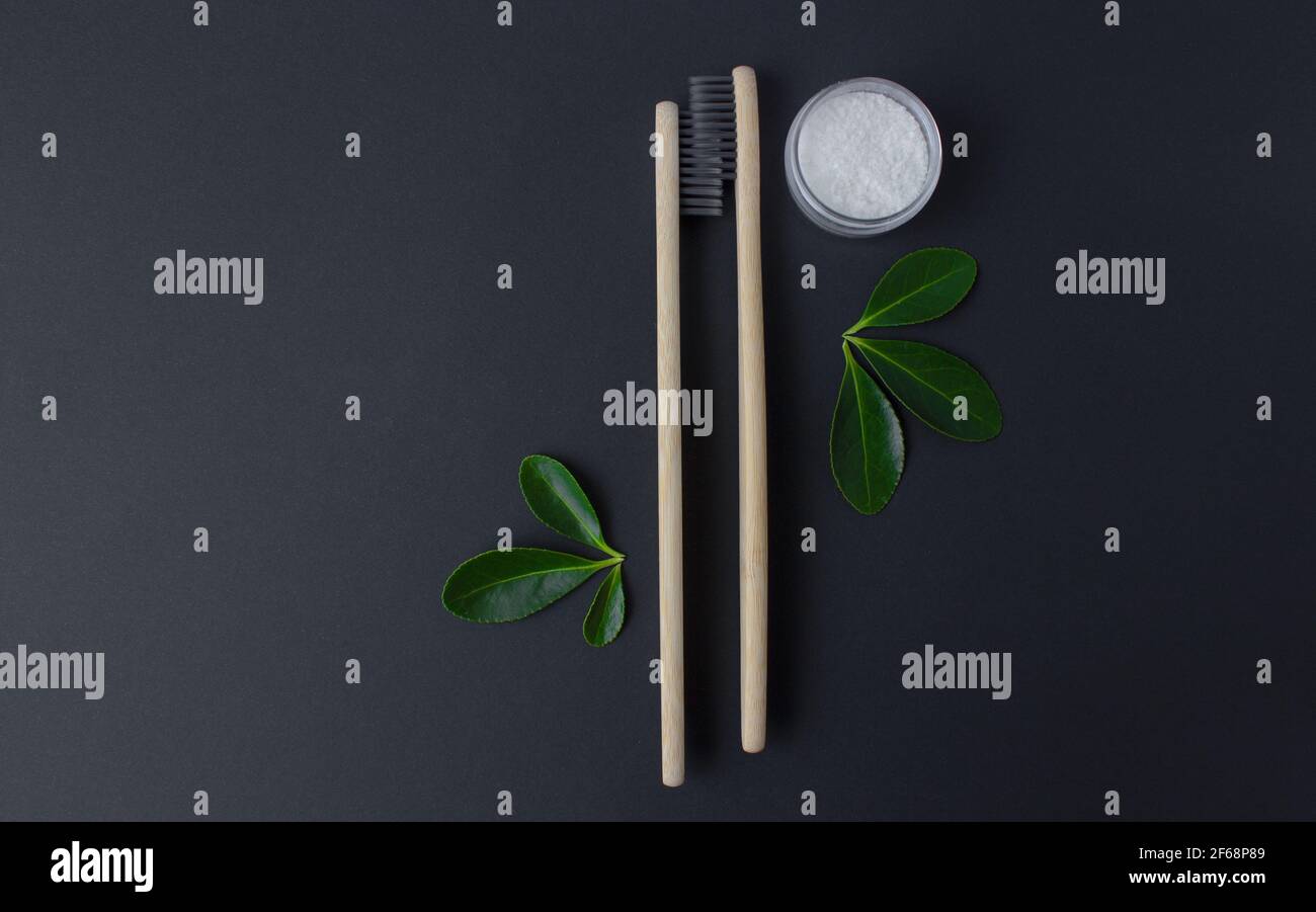 deux brosses à dents écologiques en bambou en bois, dentifrice et feuilles vertes sur fond noir. Banque D'Images