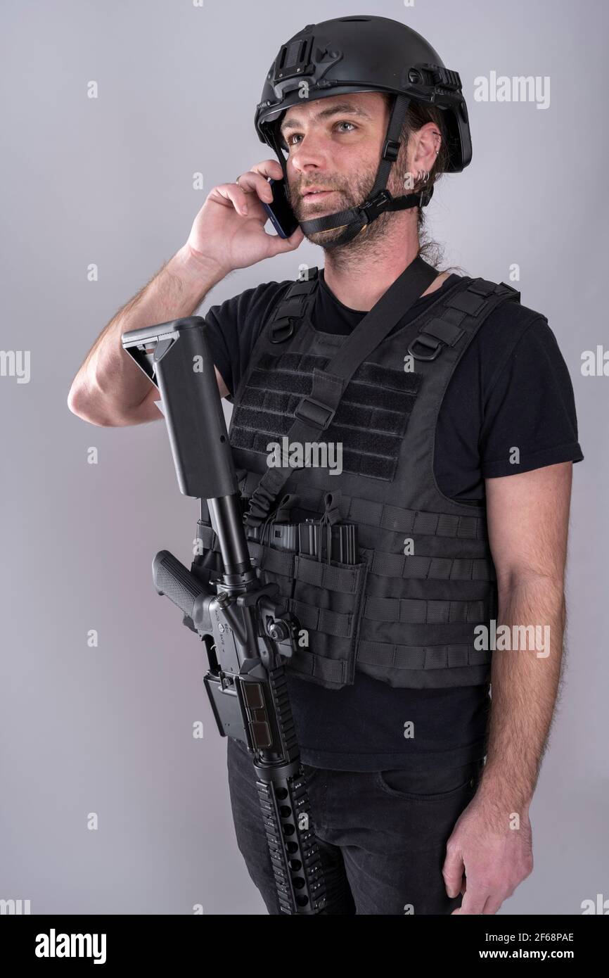 Un homme équipé pour Airsoft avec casque et gilet de protection confirme la stratégie sur le téléphone en se tenant debout avec son arme affichée. Négociation Banque D'Images
