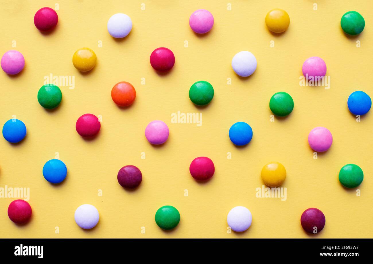 Boules de sucre colorées sur fond jaune. Bonbons au chocolat couverts de glaçage au sucre multicolore. Banque D'Images