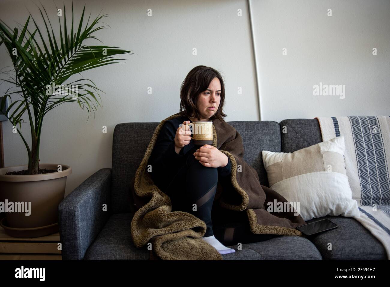 Femme assise sur un canapé avec une couverture qui avait l'air triste Banque D'Images