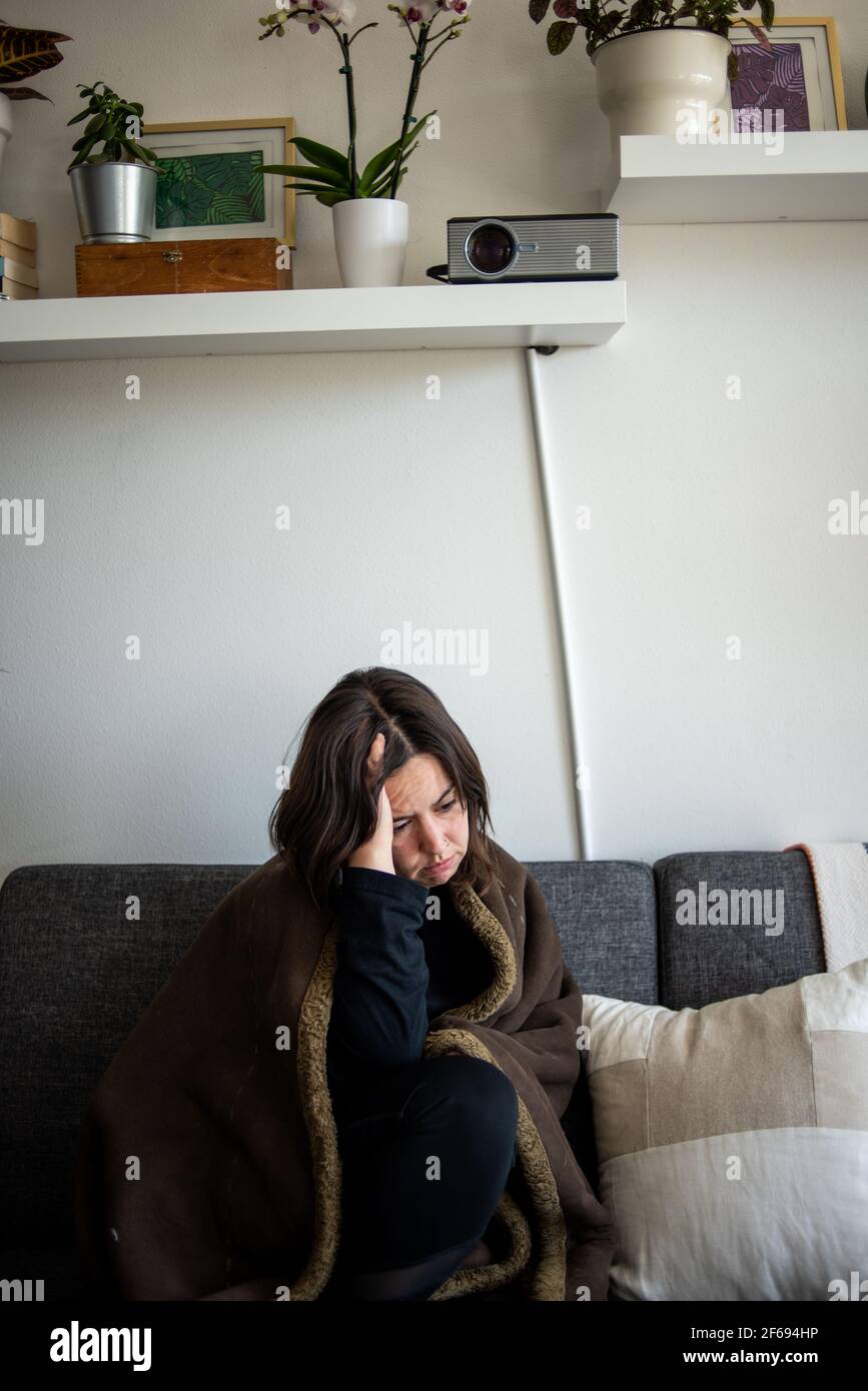 Femme assise sur un canapé sous une couverture avec la tête à la main Banque D'Images