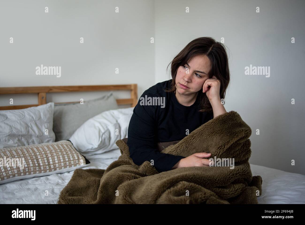 Femme assise dans un lit avec une couverture donnant sur le cadre Banque D'Images