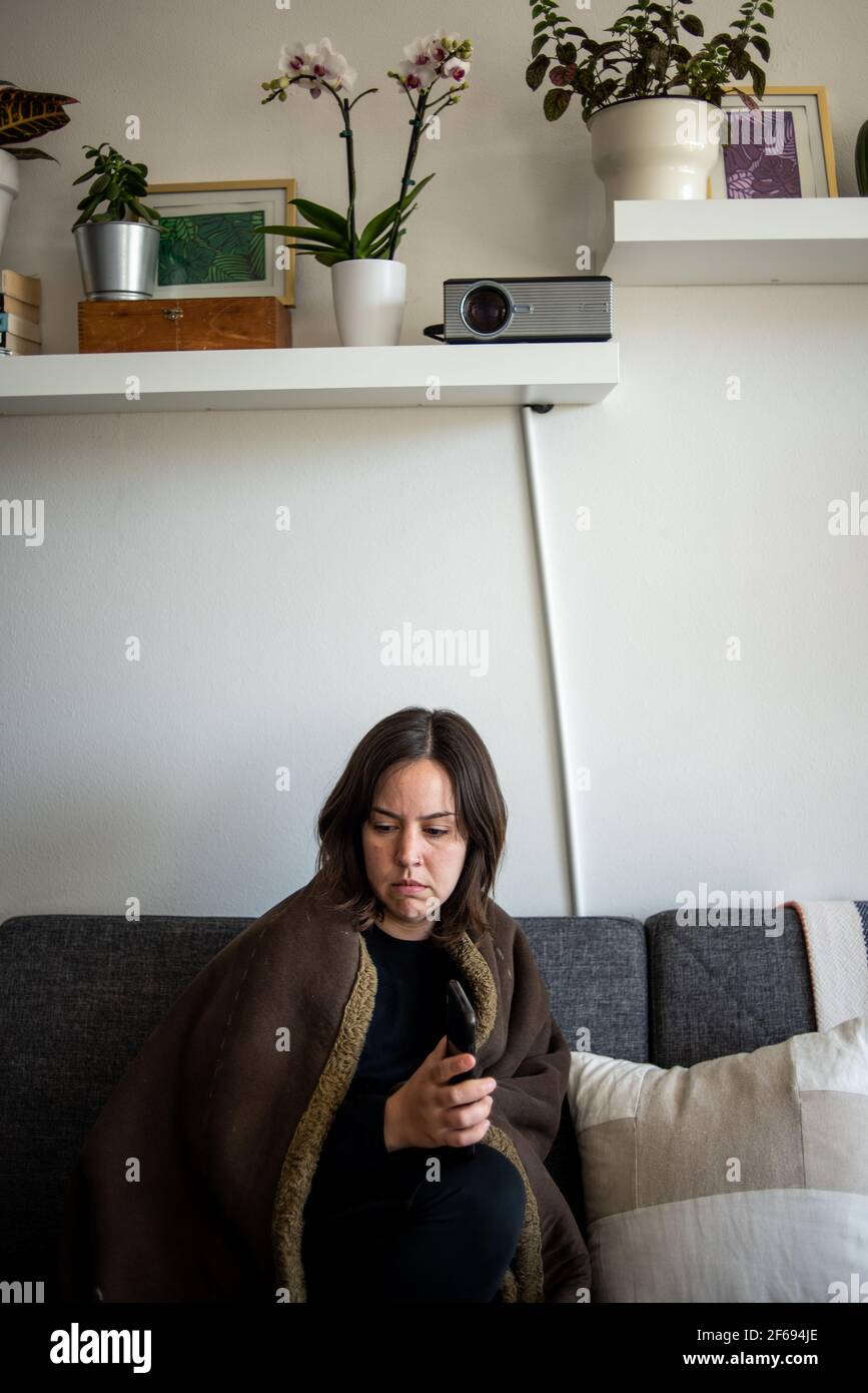 Femme enveloppée dans une couverture assise sur un canapé qui avait l'air distante Banque D'Images