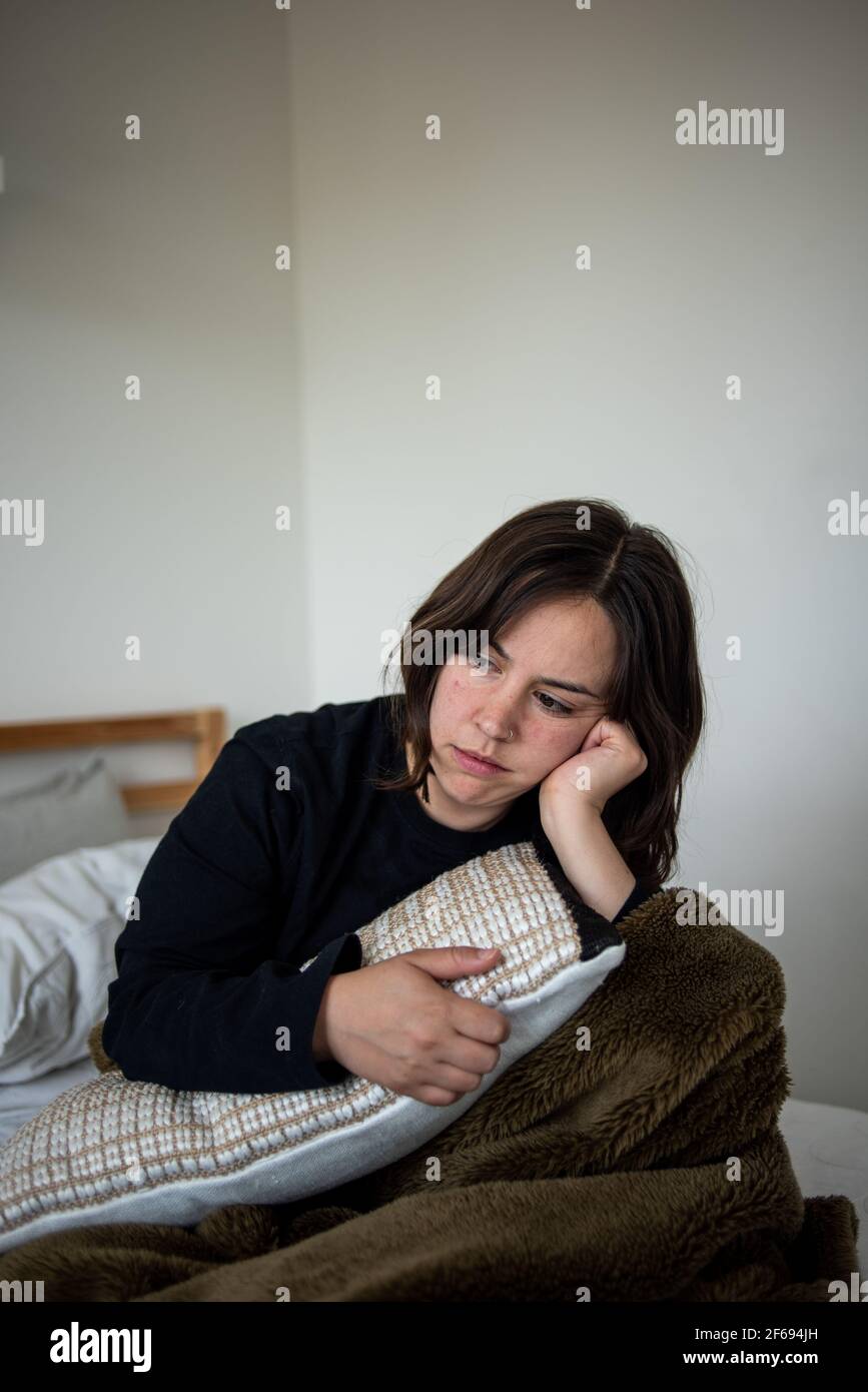 Femme assise dans un lit sous une couverture en regardant profondément dans la pensée Banque D'Images