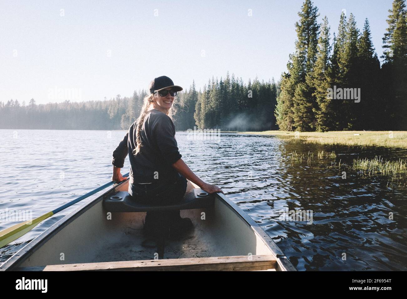 Une femme souriante regarde par-dessus son épaule tout en faisant du canoë un lac Banque D'Images