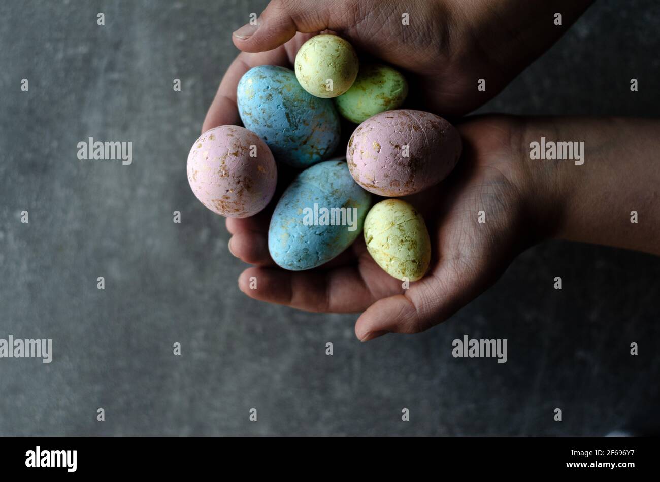 Œufs de Pâques dans les mains sur fond gris, vue du dessus Banque D'Images